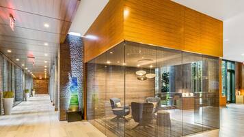 Un moderno vestíbulo de hotel con un separador de vidrio, paneles de madera y una zona de recepción con asientos.