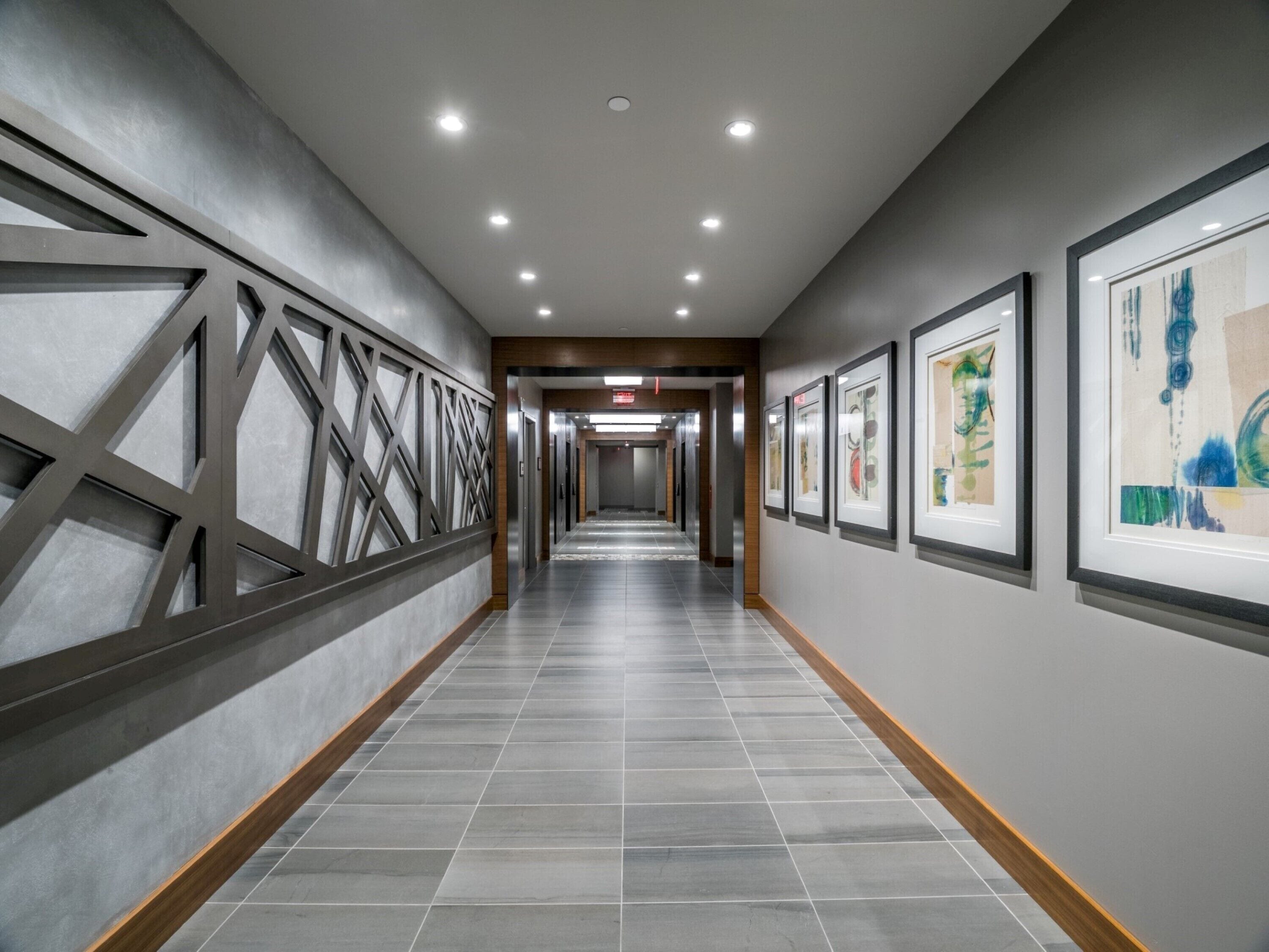 A long, narrow hallway with a tiled floor, recessed lighting, and framed artwork on the walls.