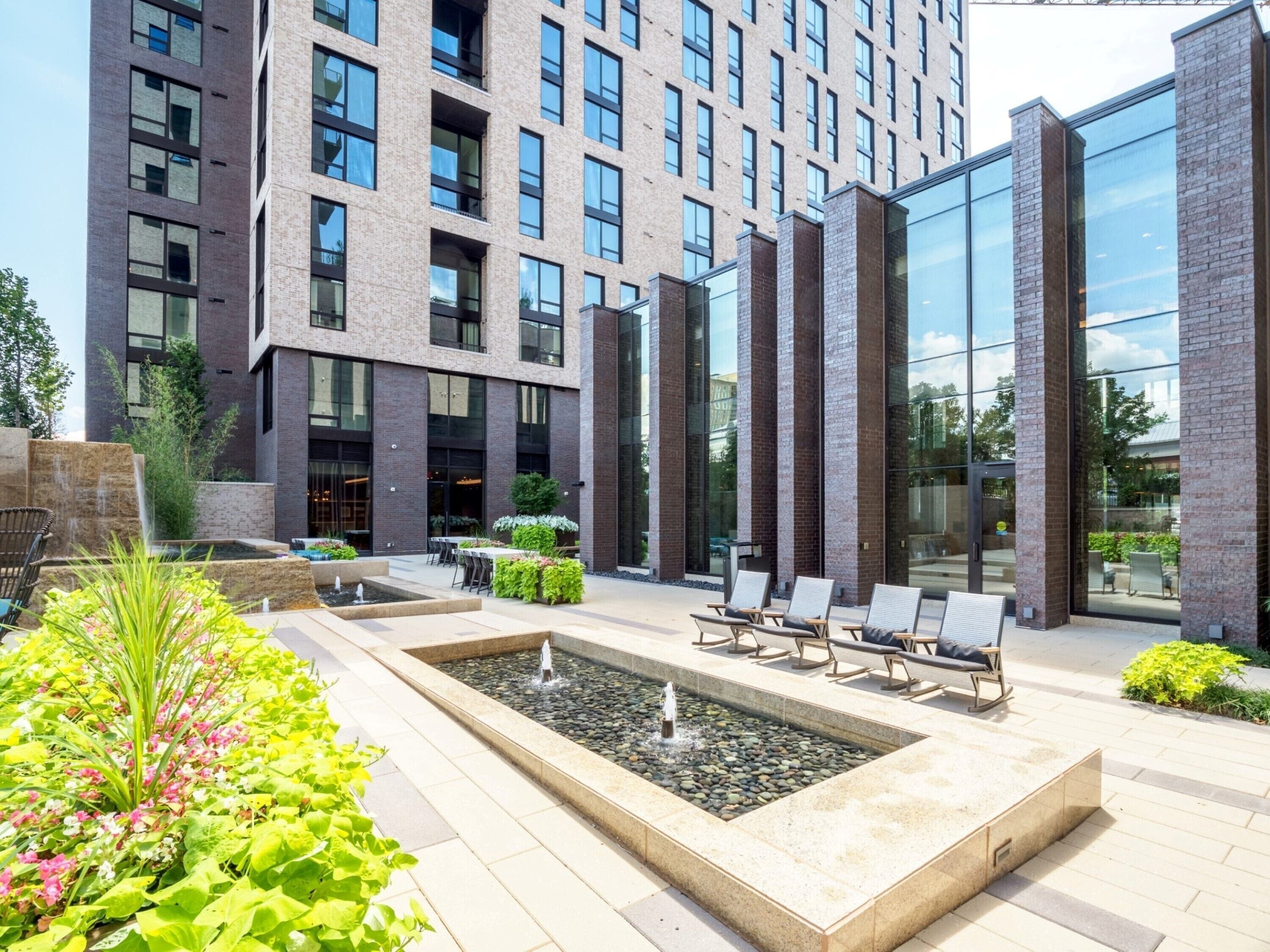 Een modern gebouw met een binnentuin, inclusief een waterpartij, zitgedeeltes en beplanting.