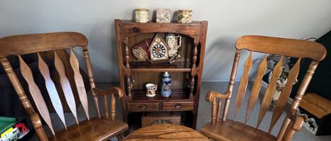 A room with a wooden chair and table, a bookshelf with decorative items, and a plain wall.