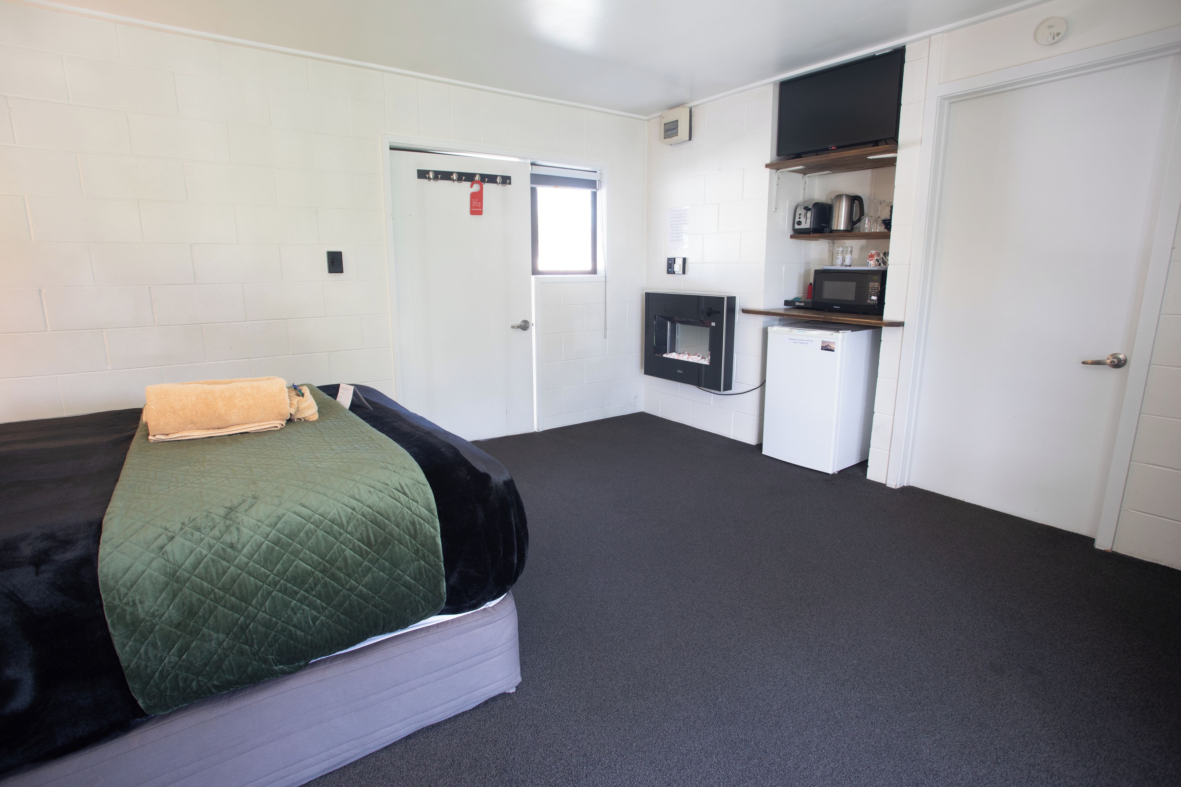 Une chambre d’hôtel de taille réduite, comprenant un lit, une petite kitchenette et une porte donnant accès à la salle de bain.
