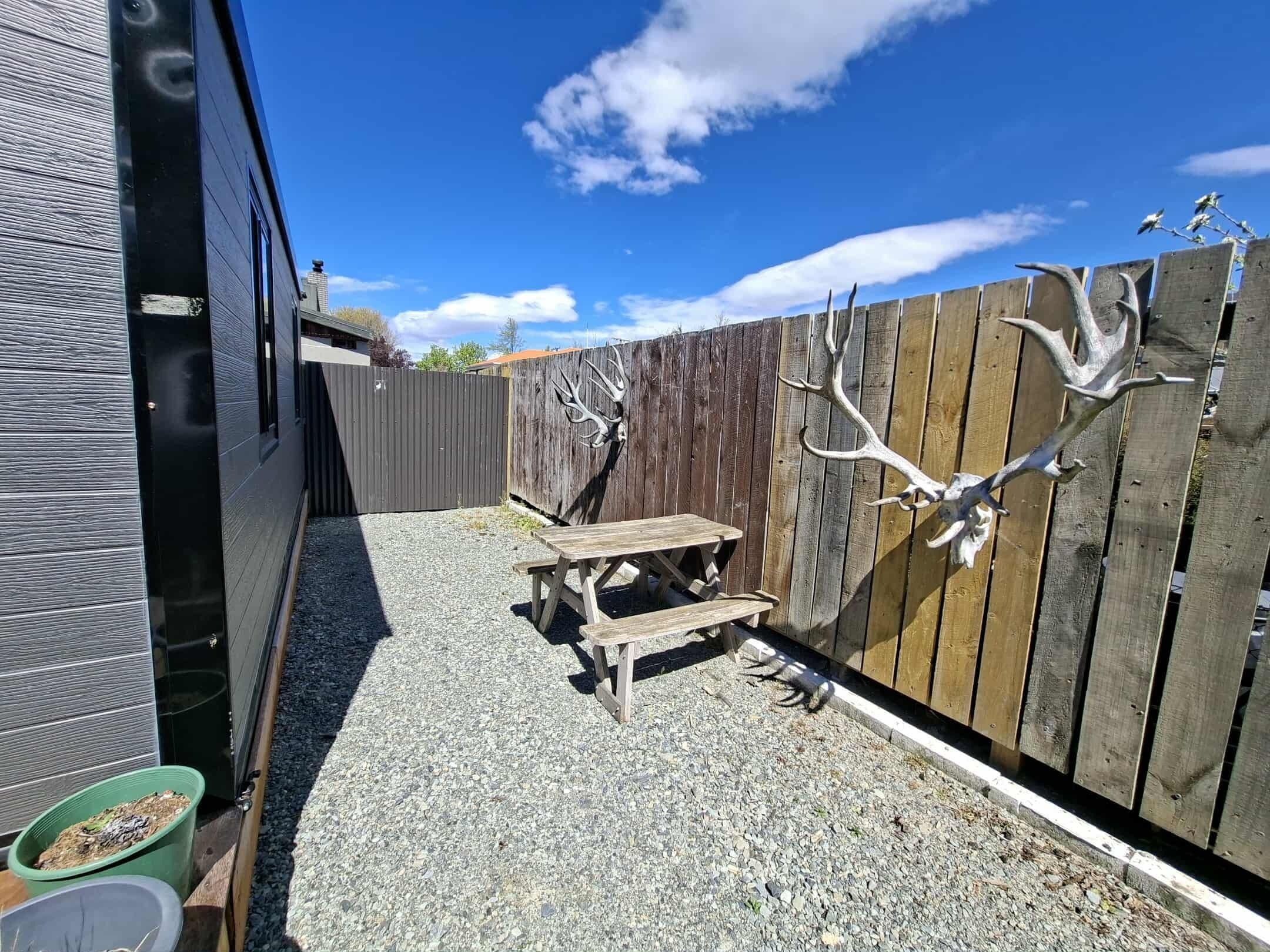 A backyard with a wooden fence, a picnic table, and a green trash bin.