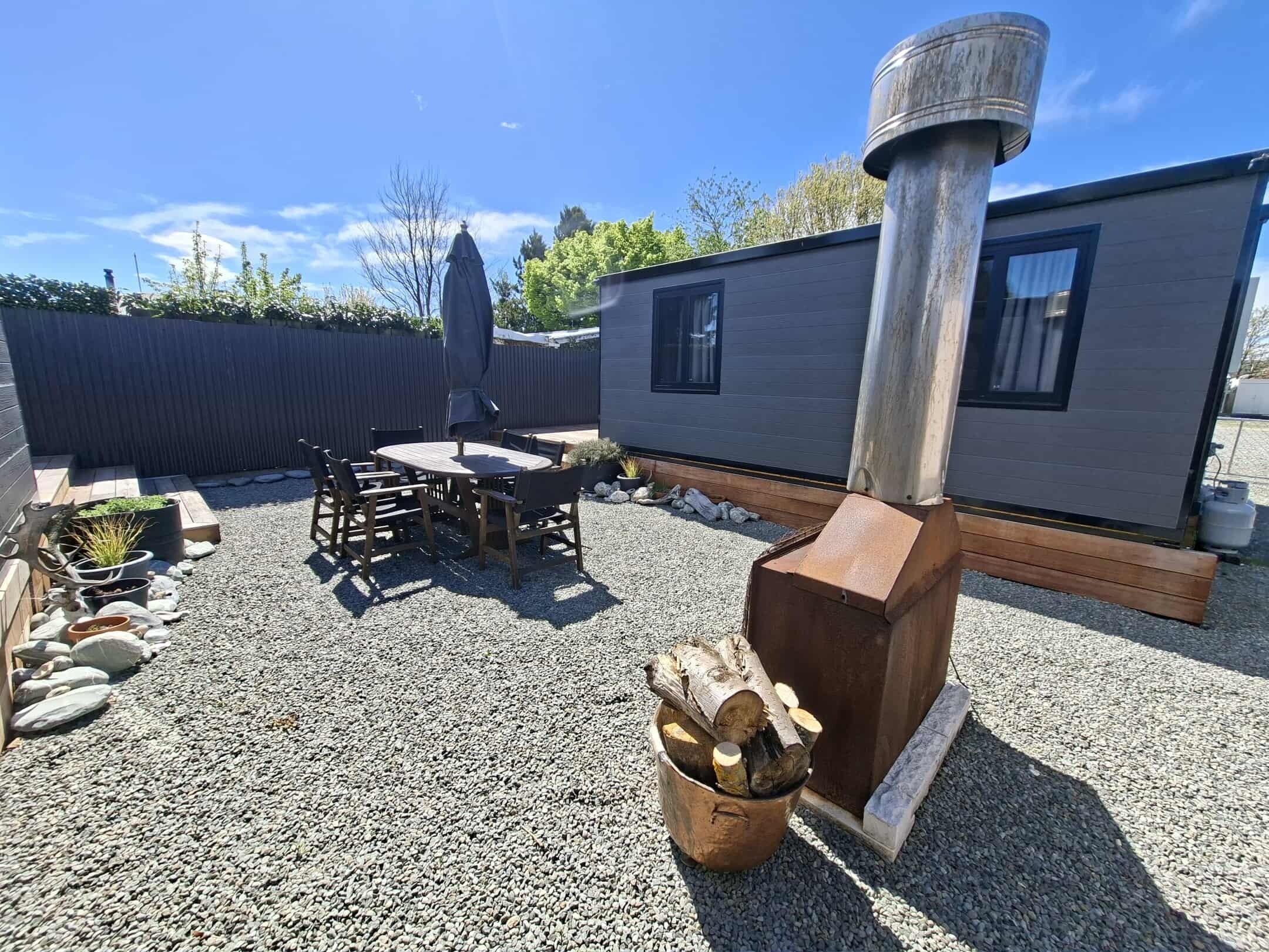 A patio area with a wooden table and chairs, a fire pit, and a small shed.