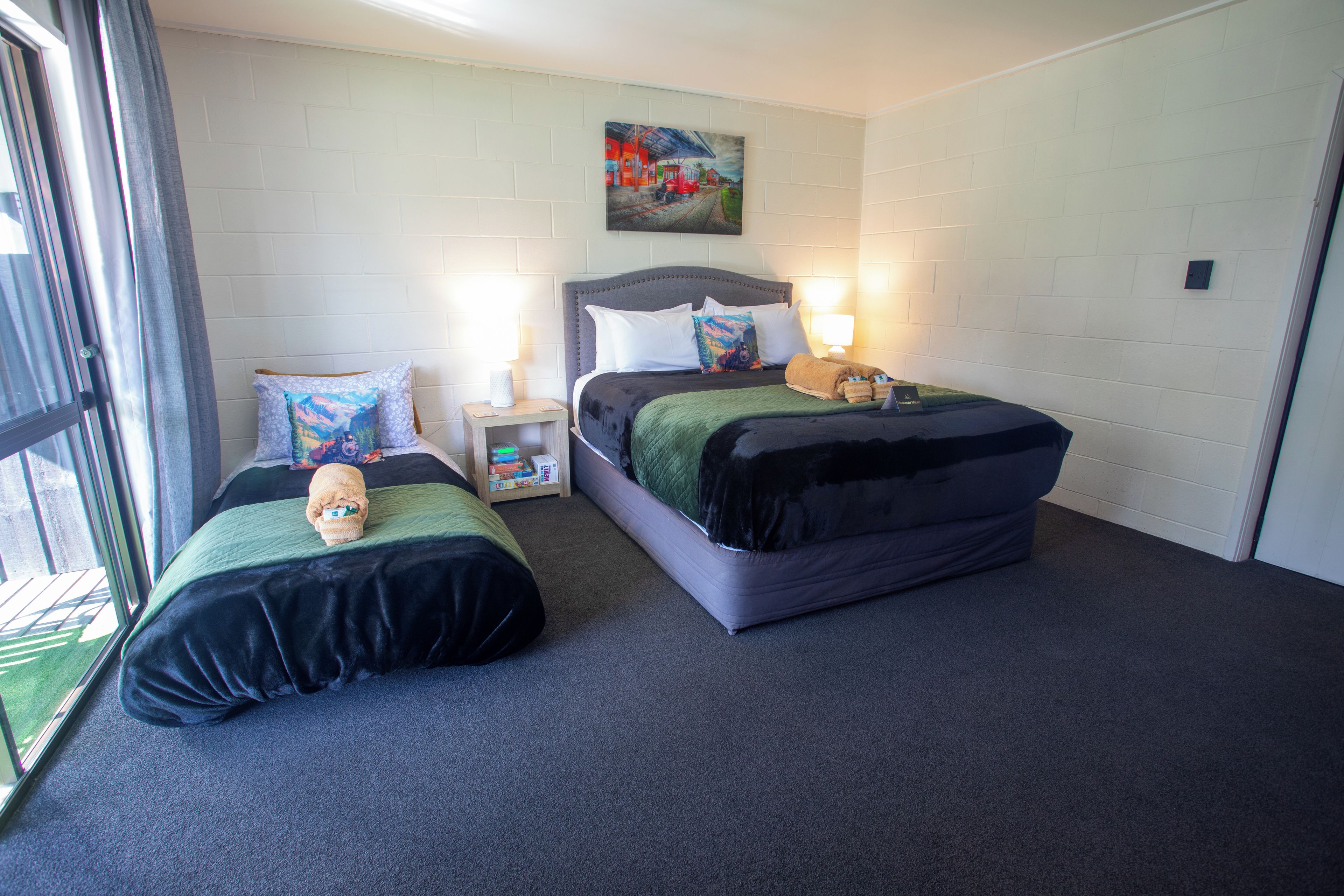 A hotel room with two beds, a painting on the wall, and a window with curtains.