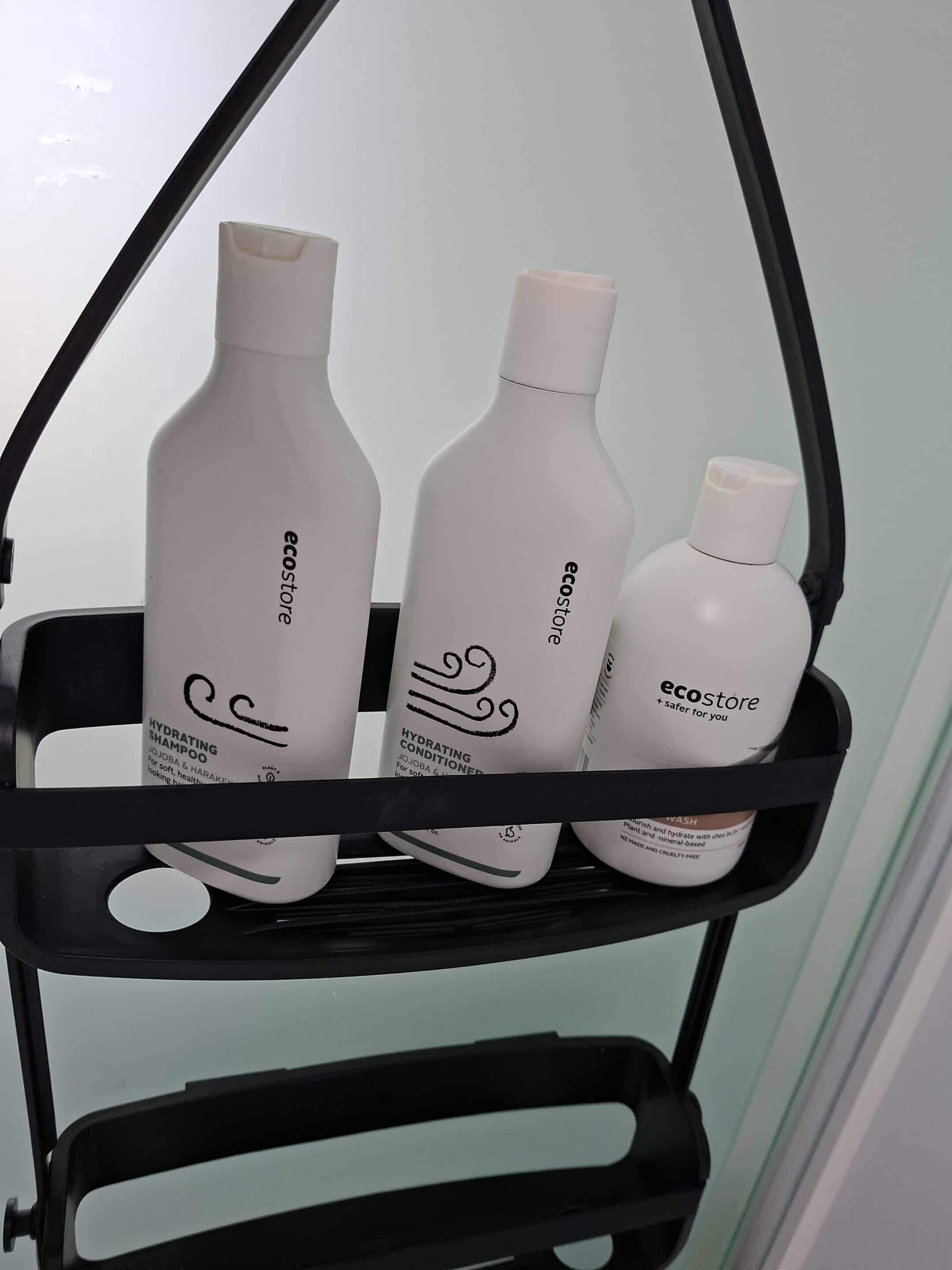 A black metal shelf with three white bottles of skincare products labeled 'ecostore'.