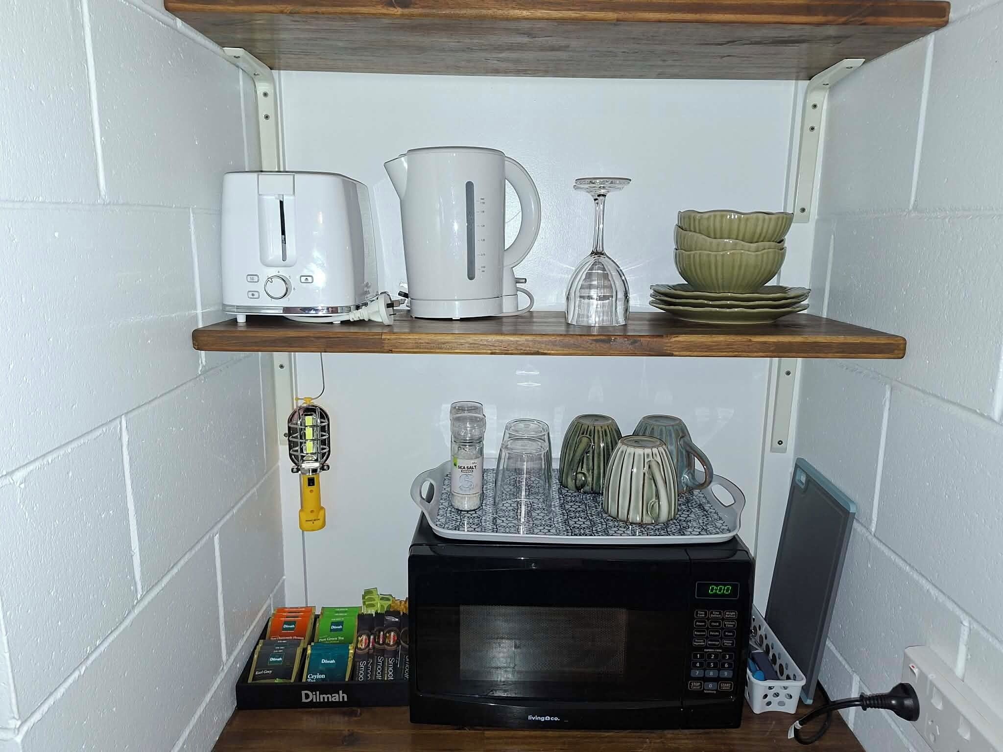 Une cuisine équipée d’un four à micro-ondes, d’un grille-pain, d’une bouilloire et d’une étagère contenant divers ustensiles de cuisine.