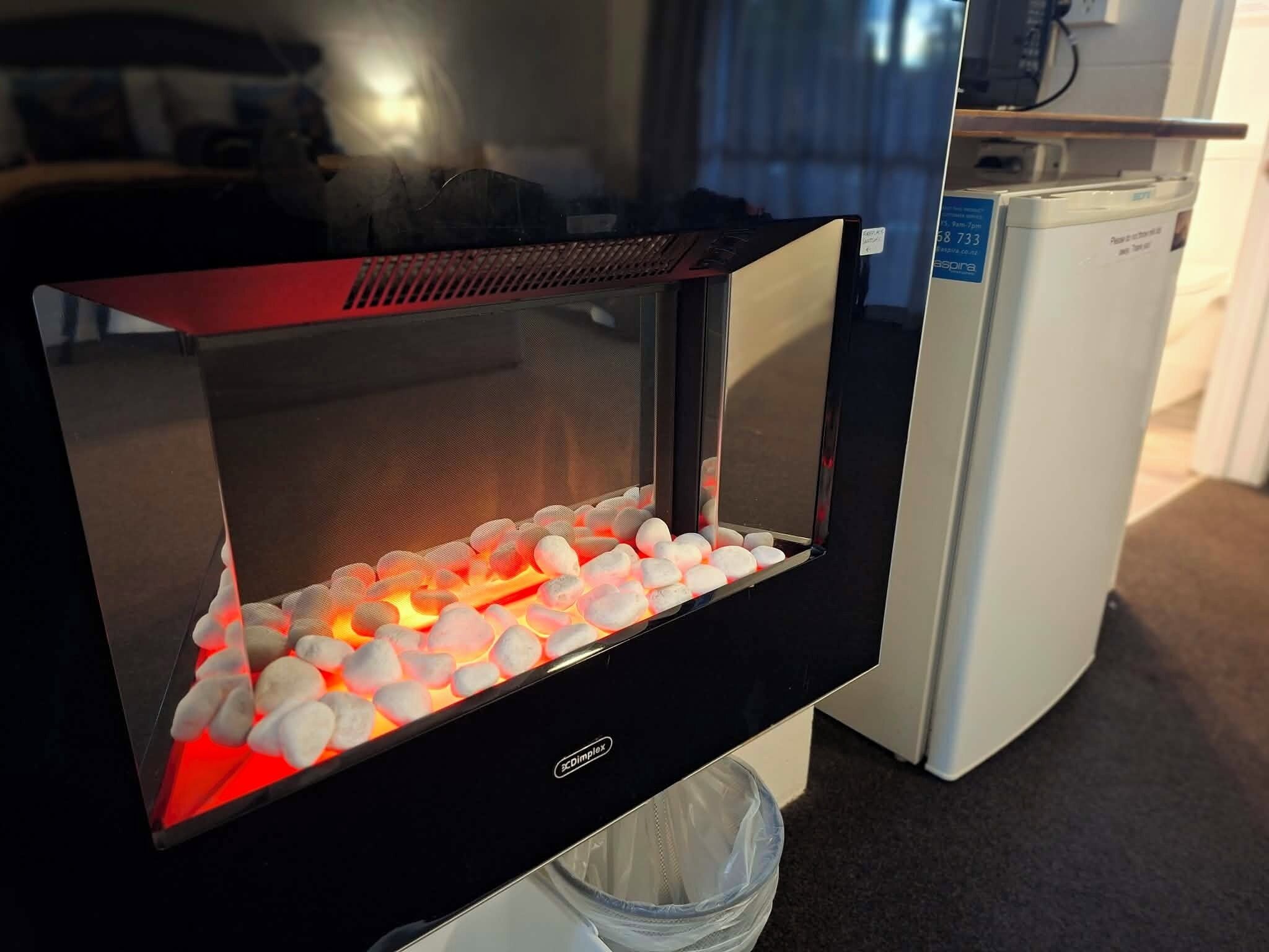 Een kamer met een zwart omlijstte televisie waarop een open haard met brandende kolen te zien is.