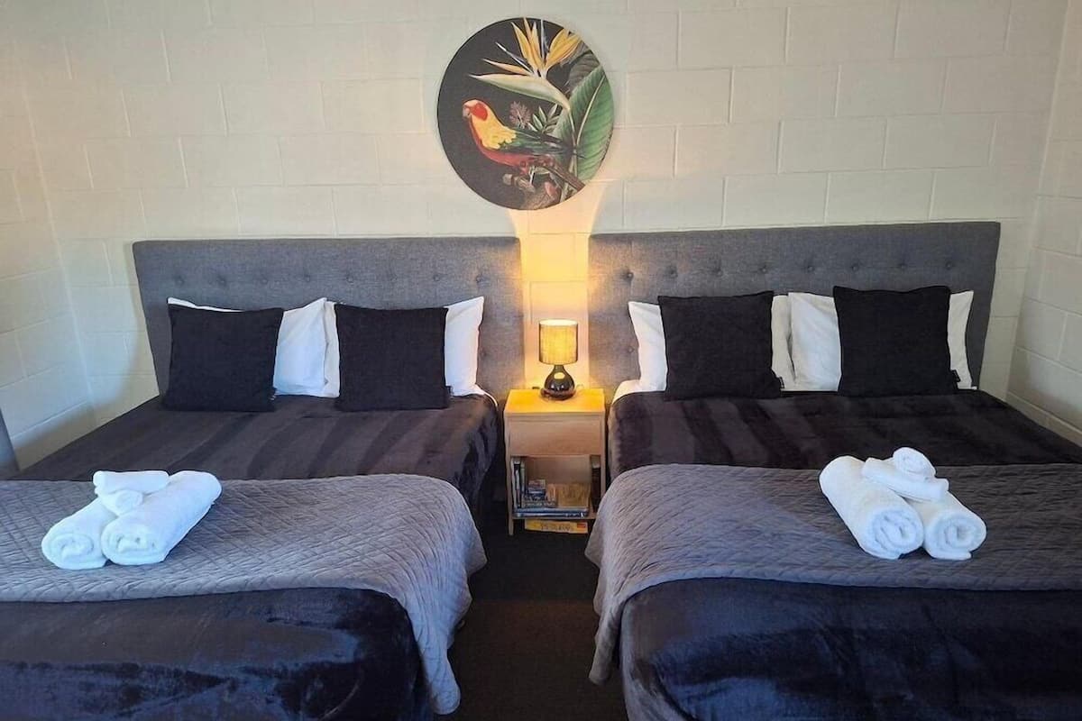 Hotellihuone, jossa on kaksi sänkyä, yöpöytä lampun kanssa ja seinällä taideteos.