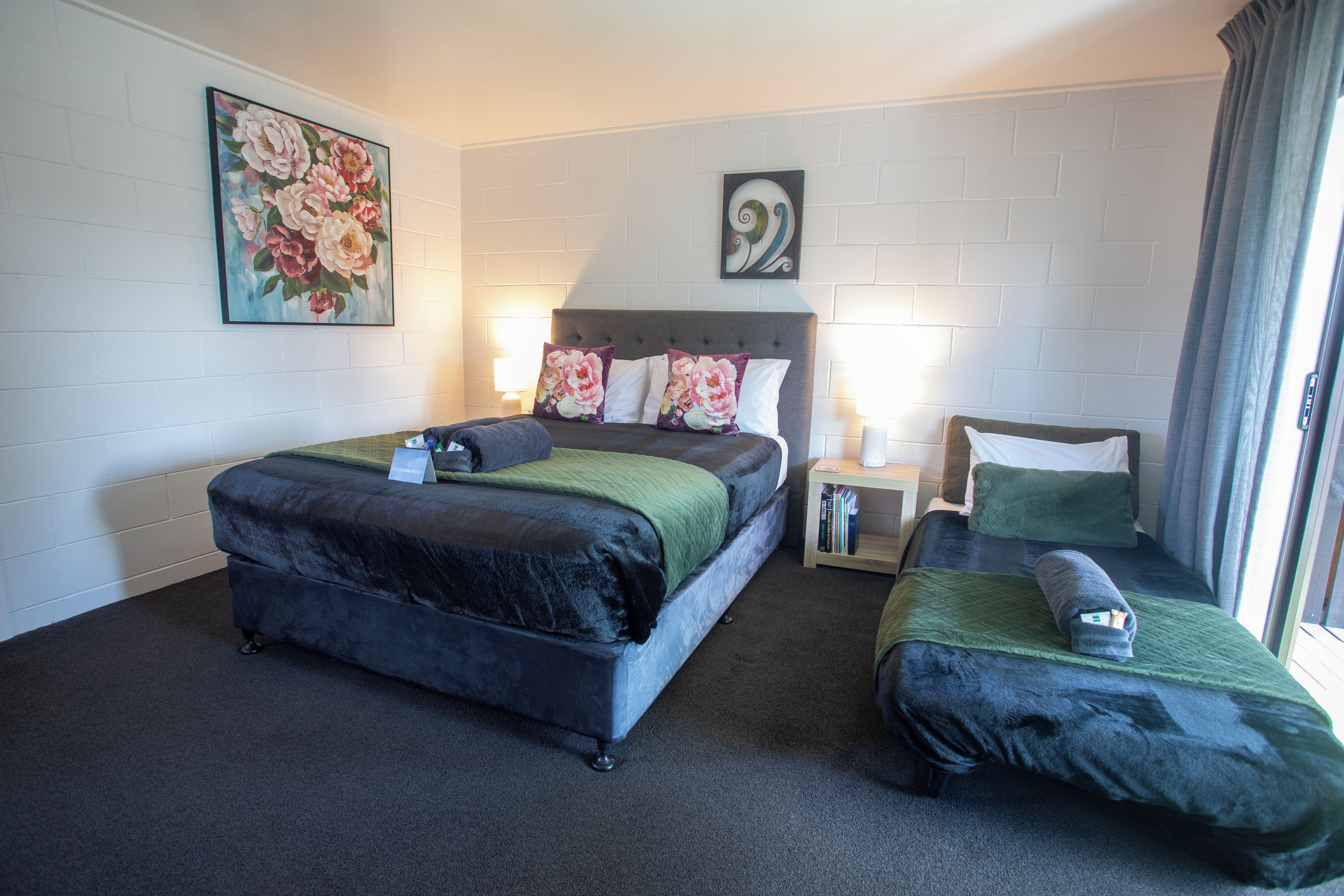 Una habitación de hotel con una cama grande, una cama más pequeña, una mesita de noche y un cuadro en la pared.