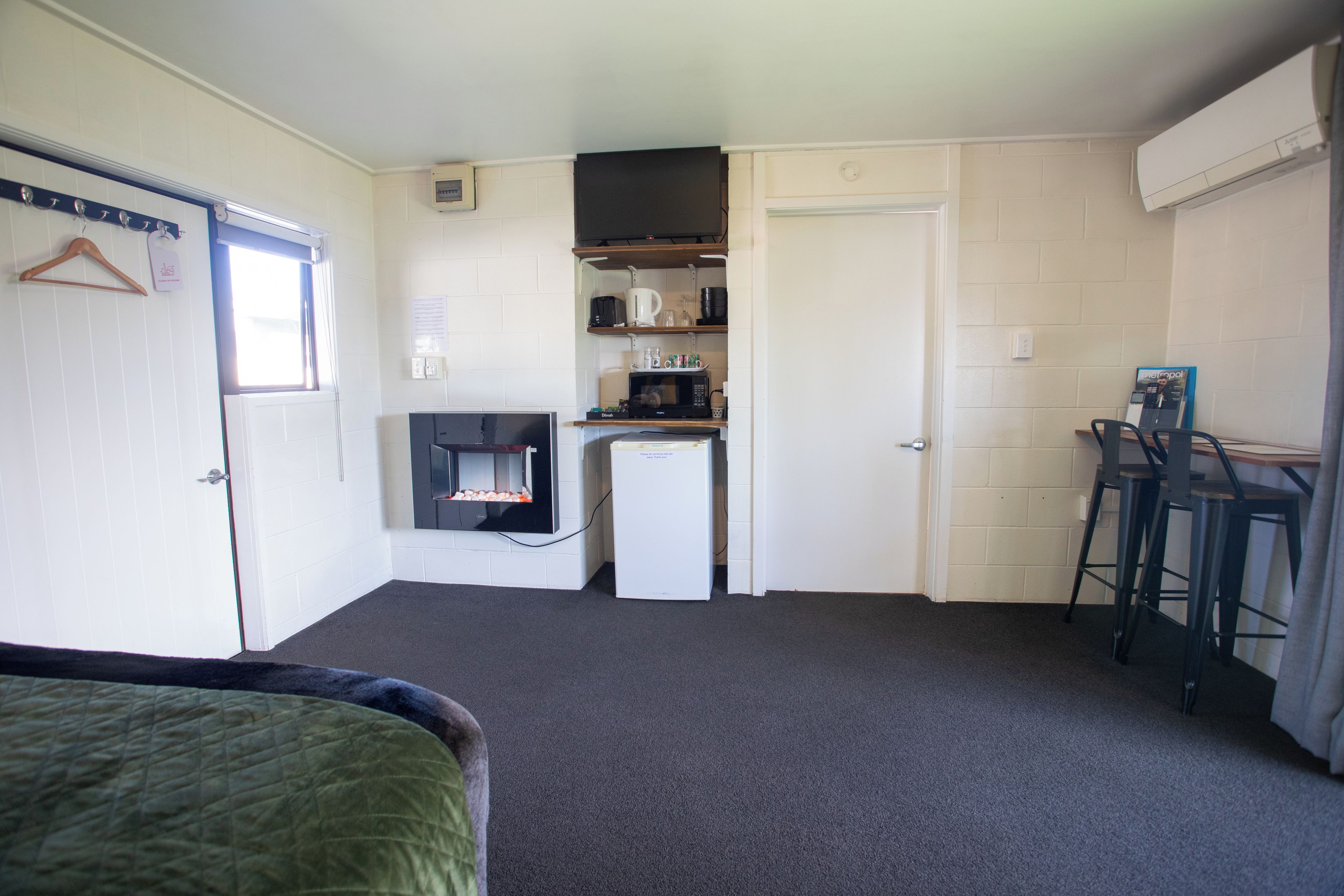A compact room with a bed, a kitchenette, a small fridge, a microwave, and a bar stool.