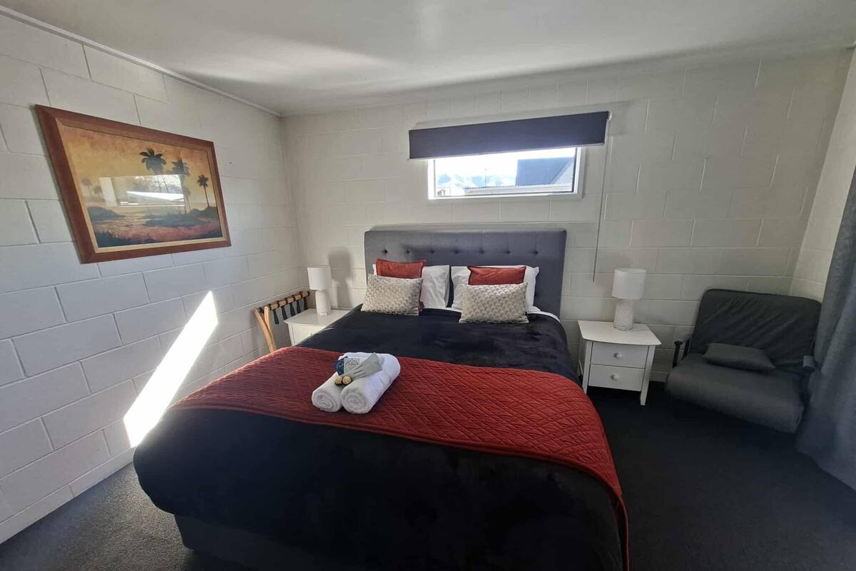 Siististi järjestetty hotellihuone, jossa on suuri sänky, tuoli, pieni pöytä ja ikkuna.