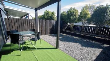 Un patio al aire libre con una mesa y sillas, rodeado por una cerca de madera y una zona de grava.