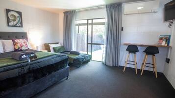 A room with a bed, a desk, two chairs, a window with curtains, a wall-mounted TV, and a magazine on the desk.