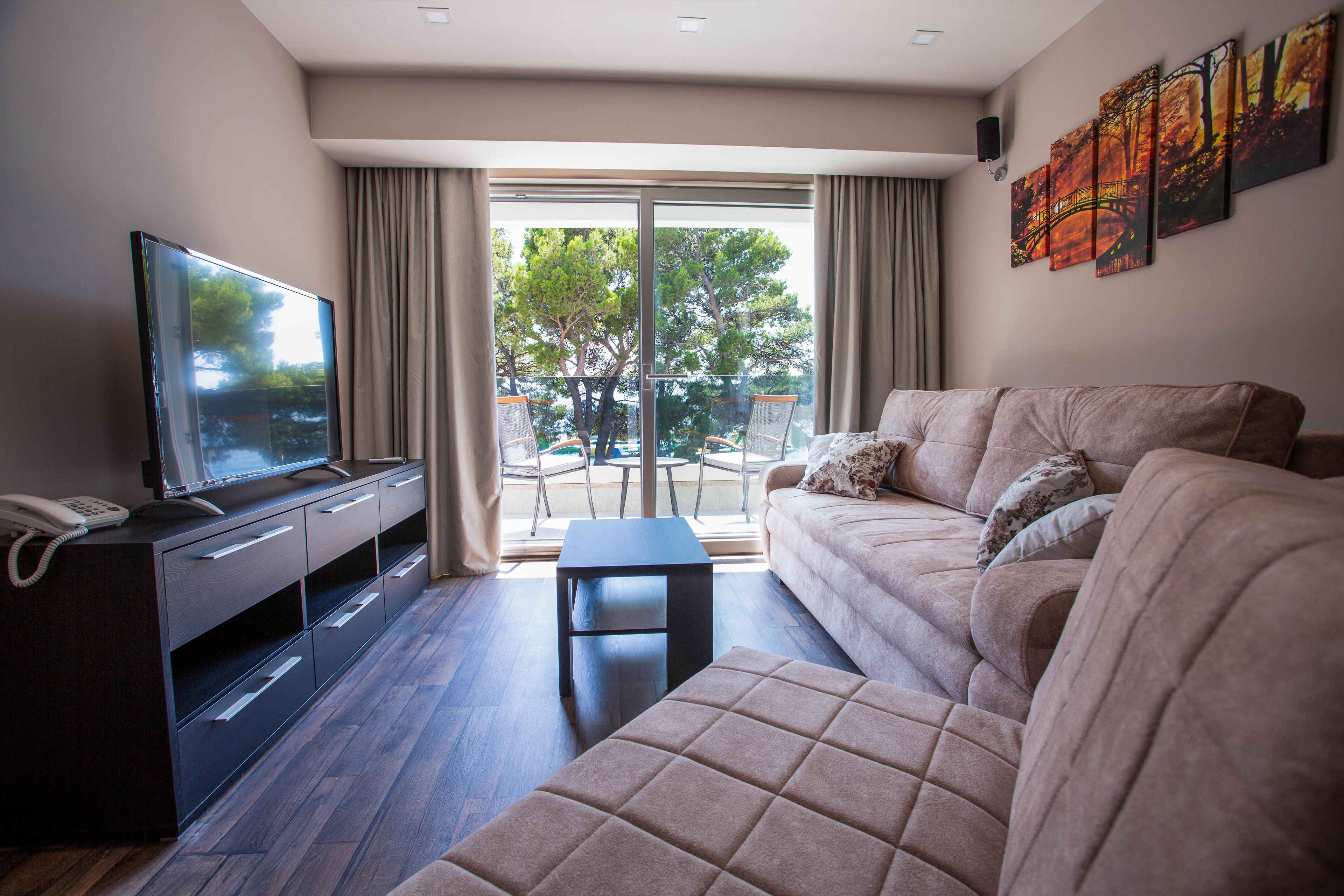 A modern living room with a sofa, a coffee table, a TV, and a sliding glass door leading to an outdoor area with chairs.