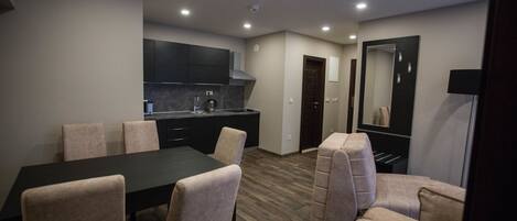 Una cocina moderna con armarios oscuros, encimera negra y estufa integrada. Hay una zona de comedor con una mesa negra y sillas color beige.