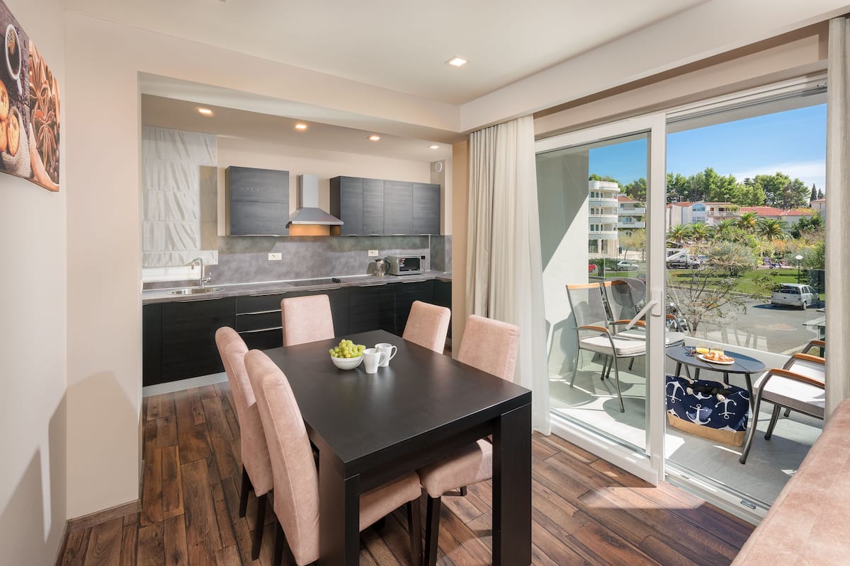 A modern kitchen with dark cabinets, a dining table with chairs, and a view of a balcony with outdoor seating.