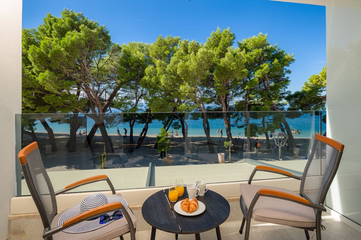 A balcony with two chairs, a small table, and a view of the beach and sea.