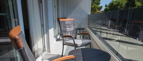 A balcony with two chairs and a small table, large windows, and a view of trees and buildings.