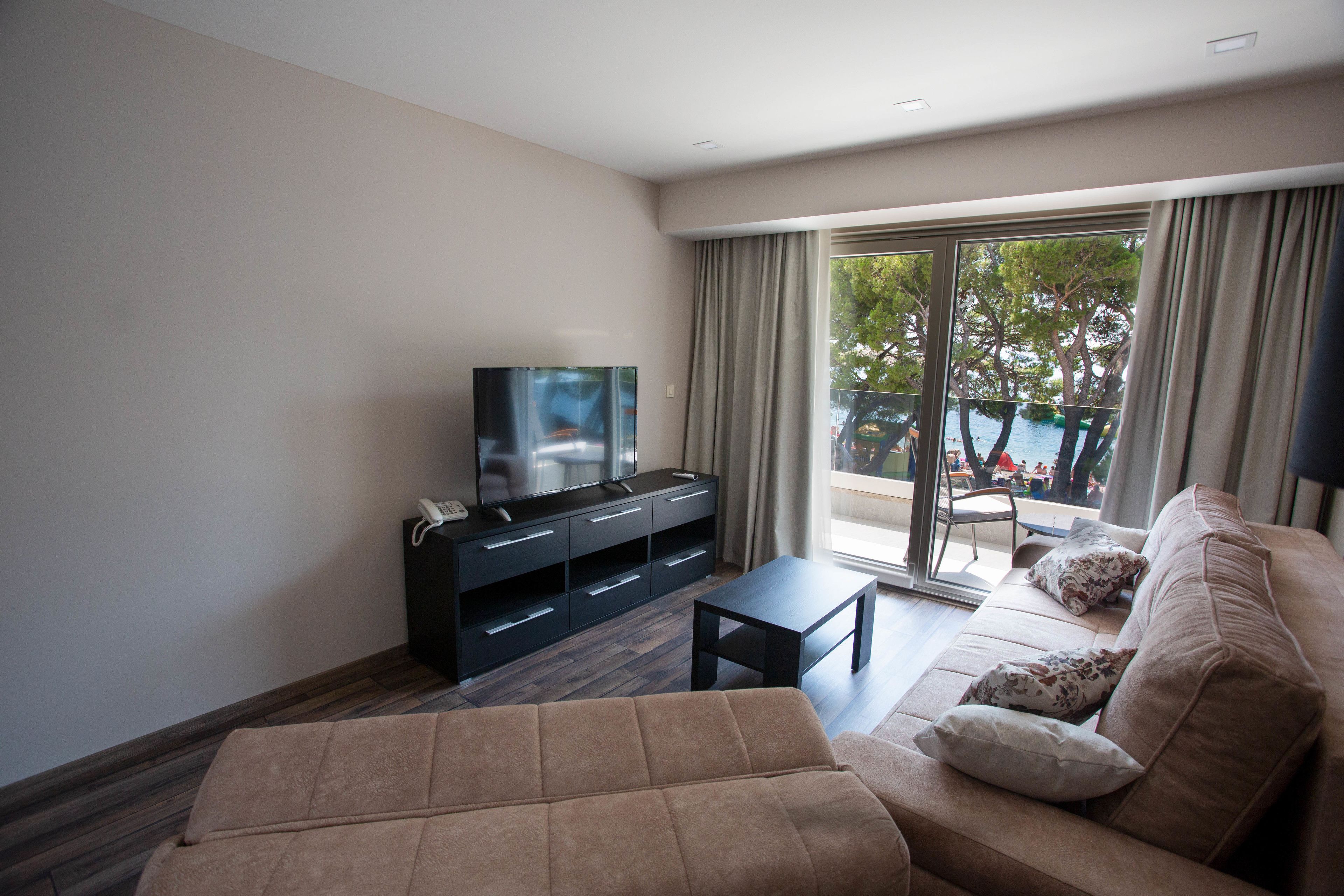 A modern living room with a sofa, a TV, and a balcony with a pool view.