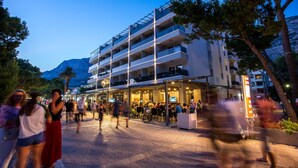 Un hotel de varios pisos con terraza exterior y montañas al fondo.
