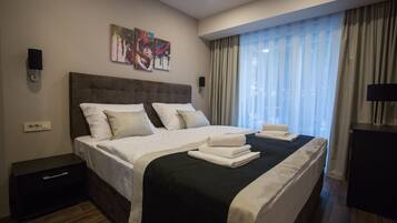 A modern hotel room with a large bed, a nightstand, a desk, and a window with curtains.