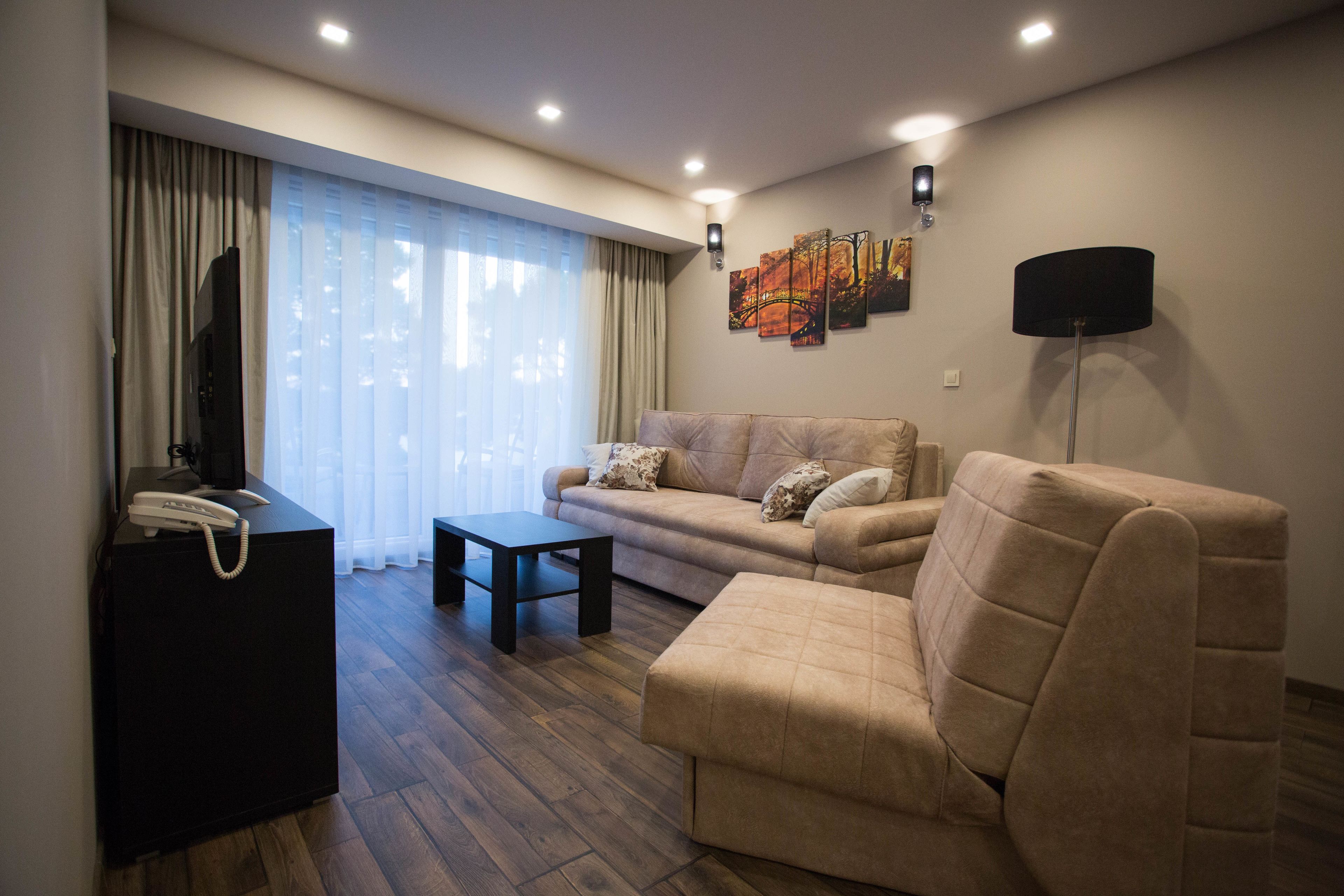Una sala de estar moderna con un sofá, un reposapiés y una mesita. Hay un televisor de pantalla plana sobre un mueble, una lámpara y una obra de arte en la pared.