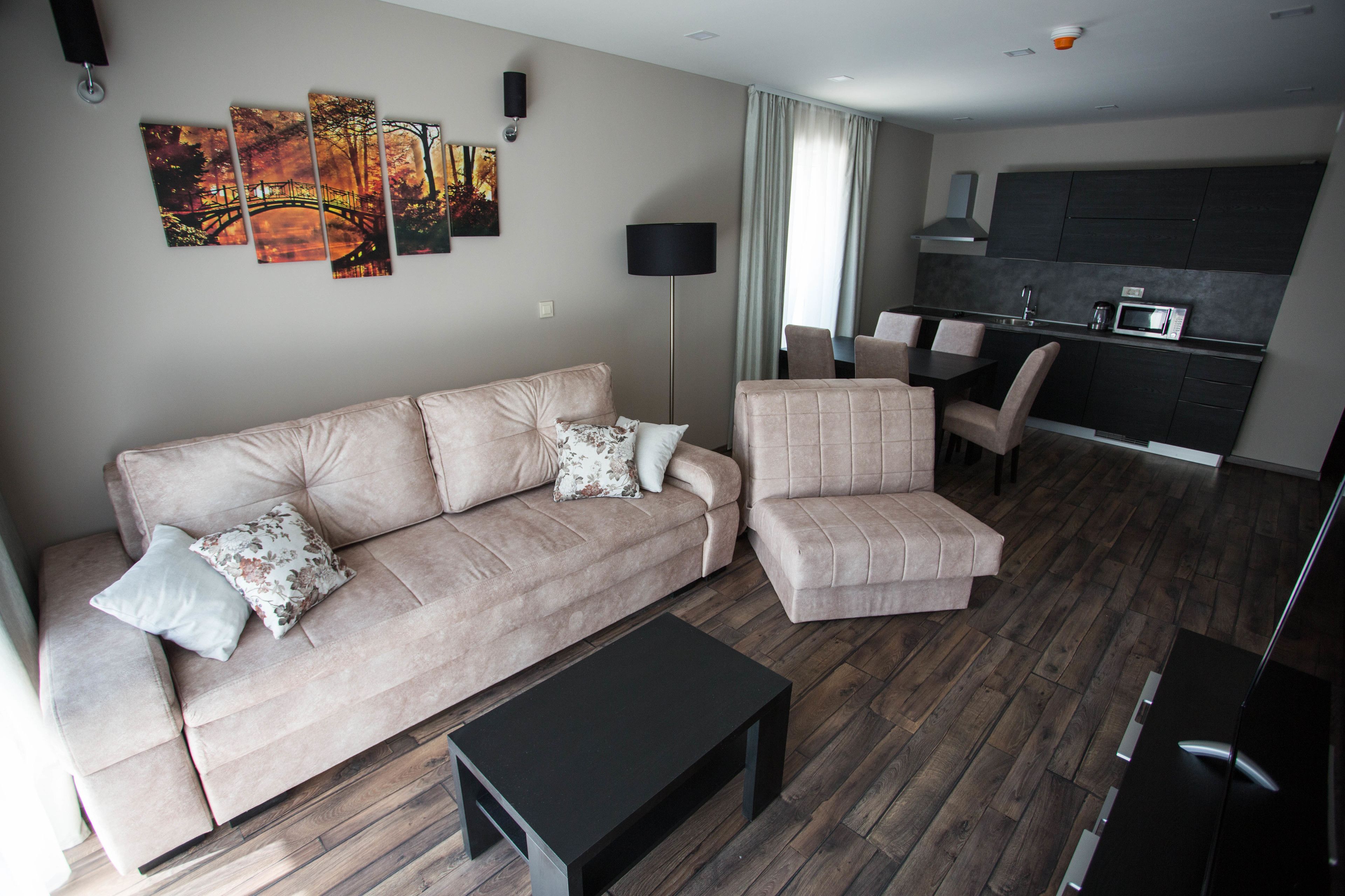 A modern living room with a sofa, armchair, and coffee table. A kitchen area is visible in the background.