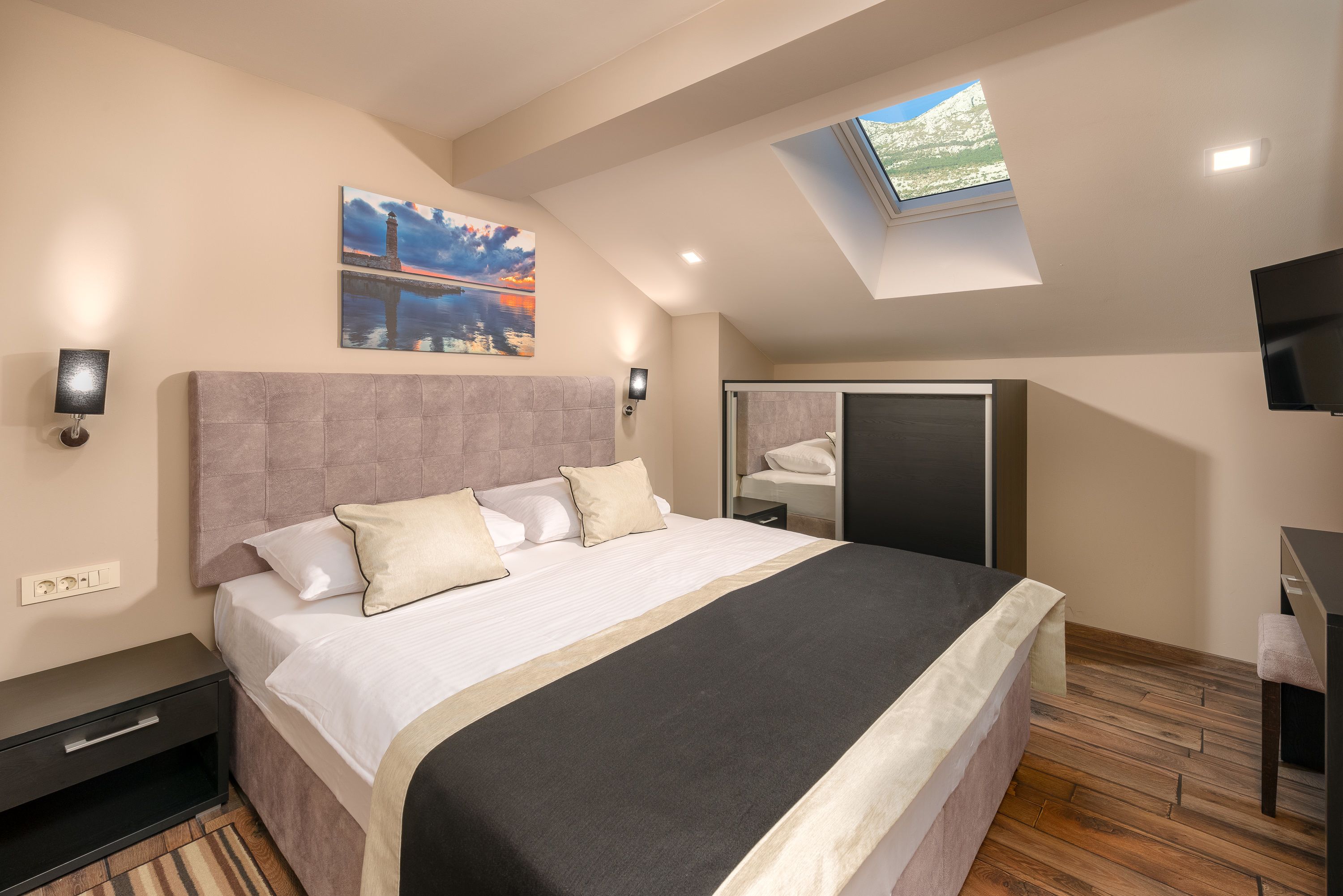 A bedroom with a large bed, a skylight, a painting, a TV, and a wardrobe.