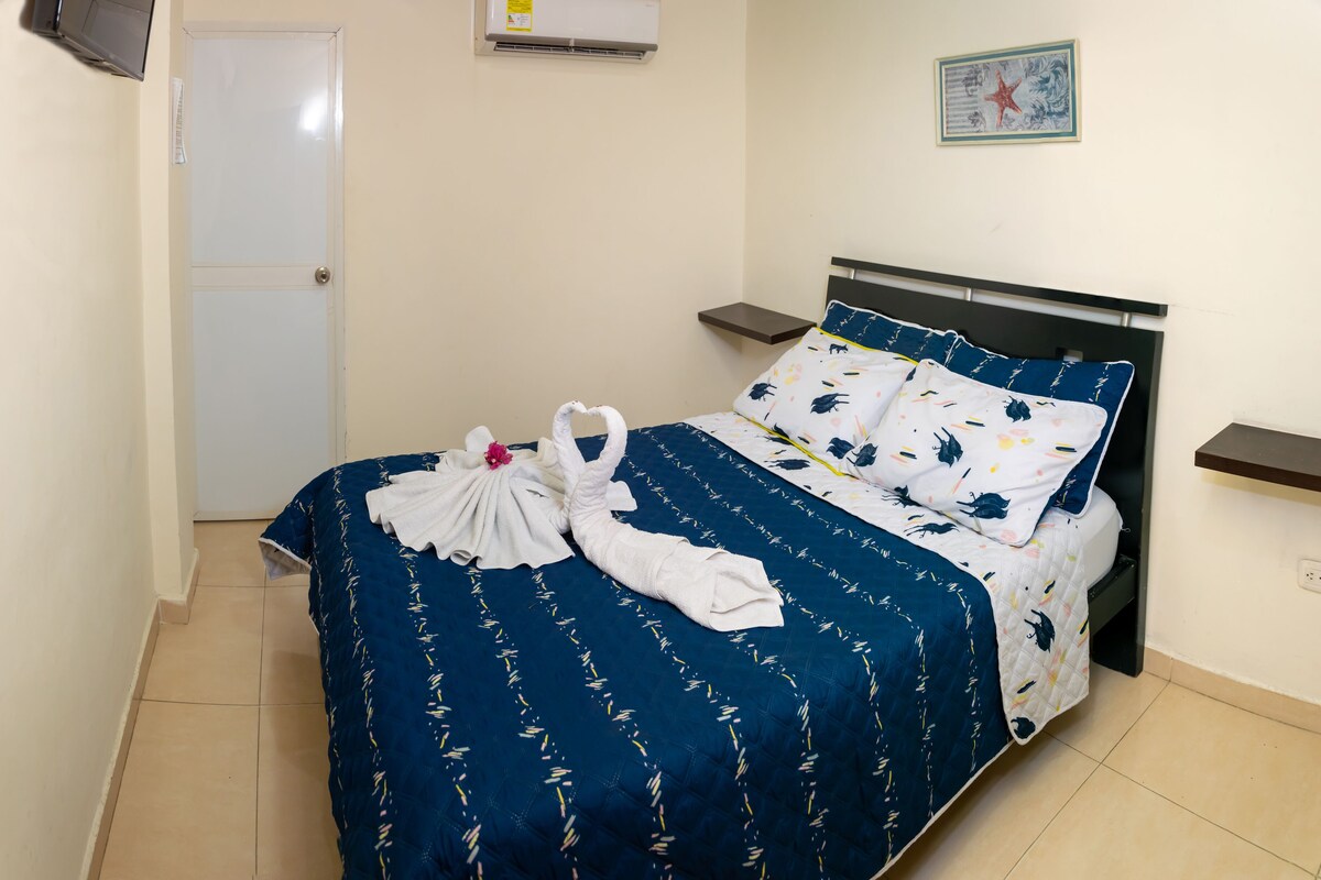 A neatly made bed with a blue and white floral bedspread, two pillows, and a decorative towel arrangement.