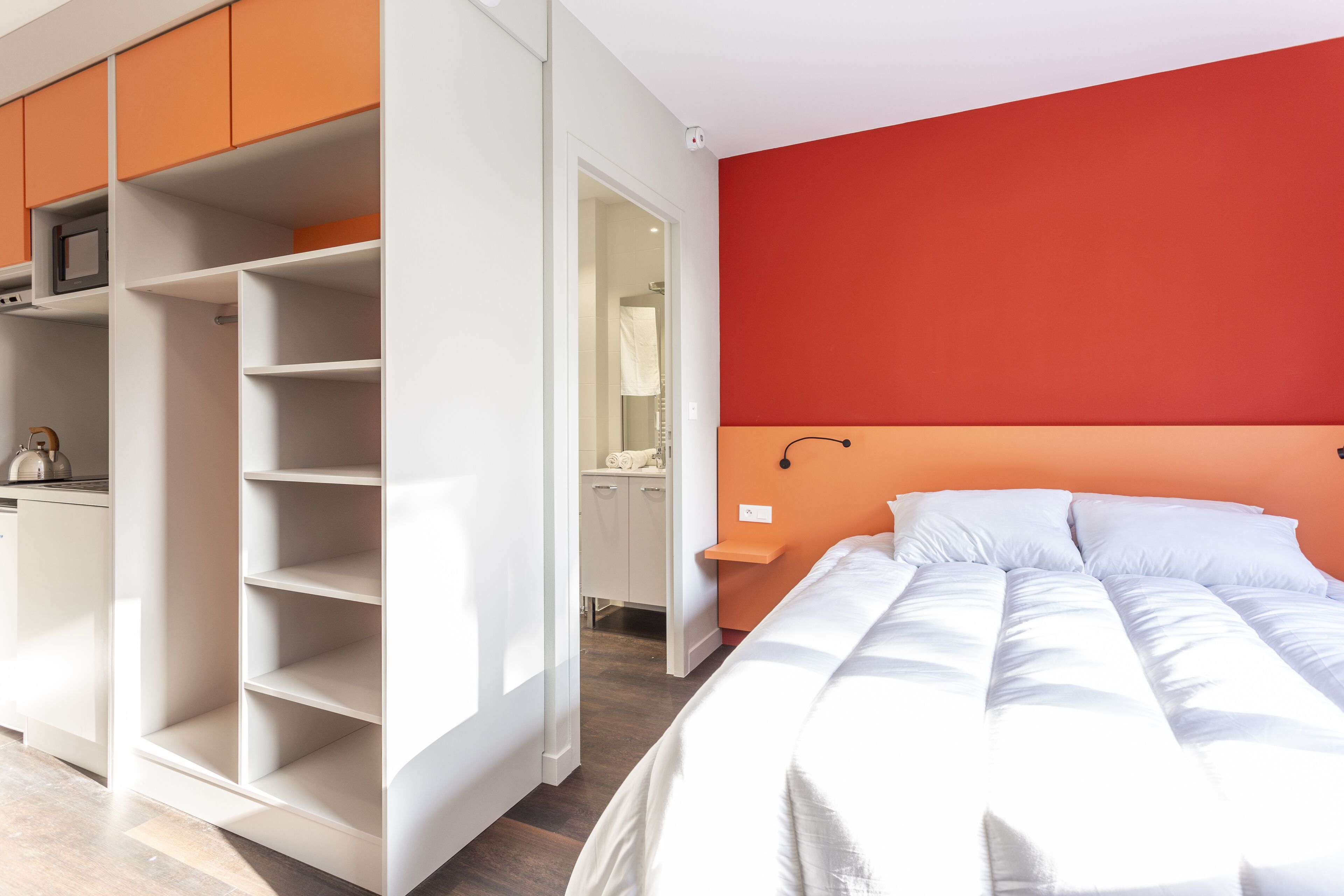A bedroom with a bed, a wardrobe, and a red accent wall.