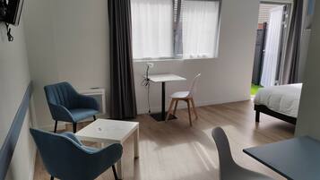Habitación de hotel con cama, escritorio, dos sillas, una mesita y una ventana con cortinas.
