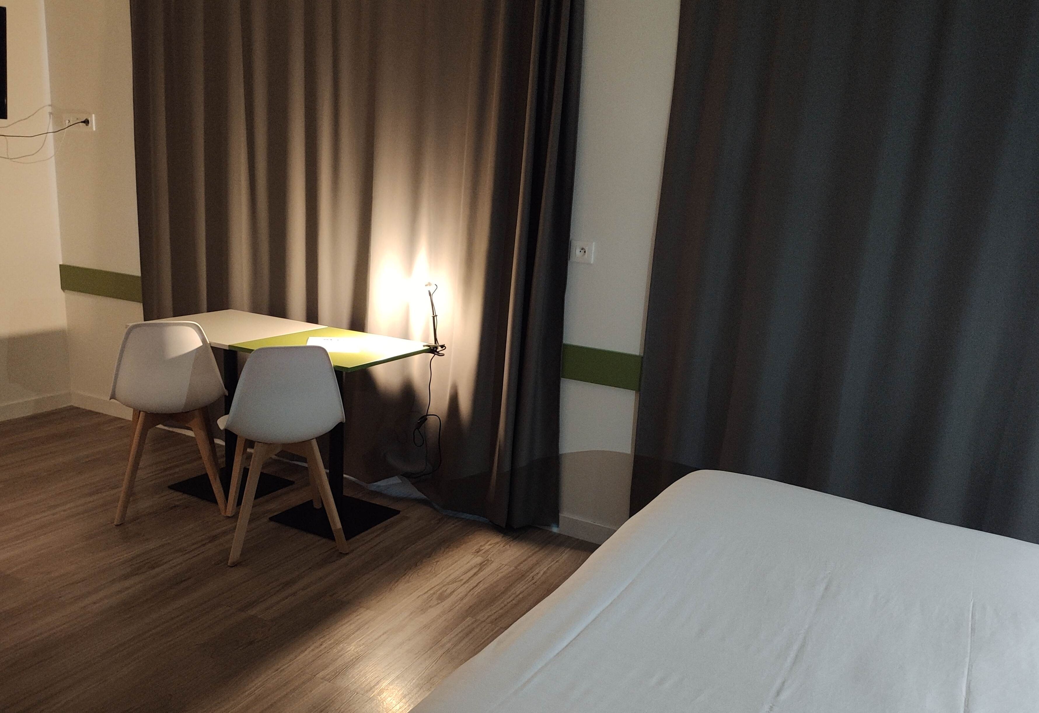 Ein Hotelzimmer mit einem Bett, einem Schreibtisch mit zwei Stühlen und einem Vorhang.