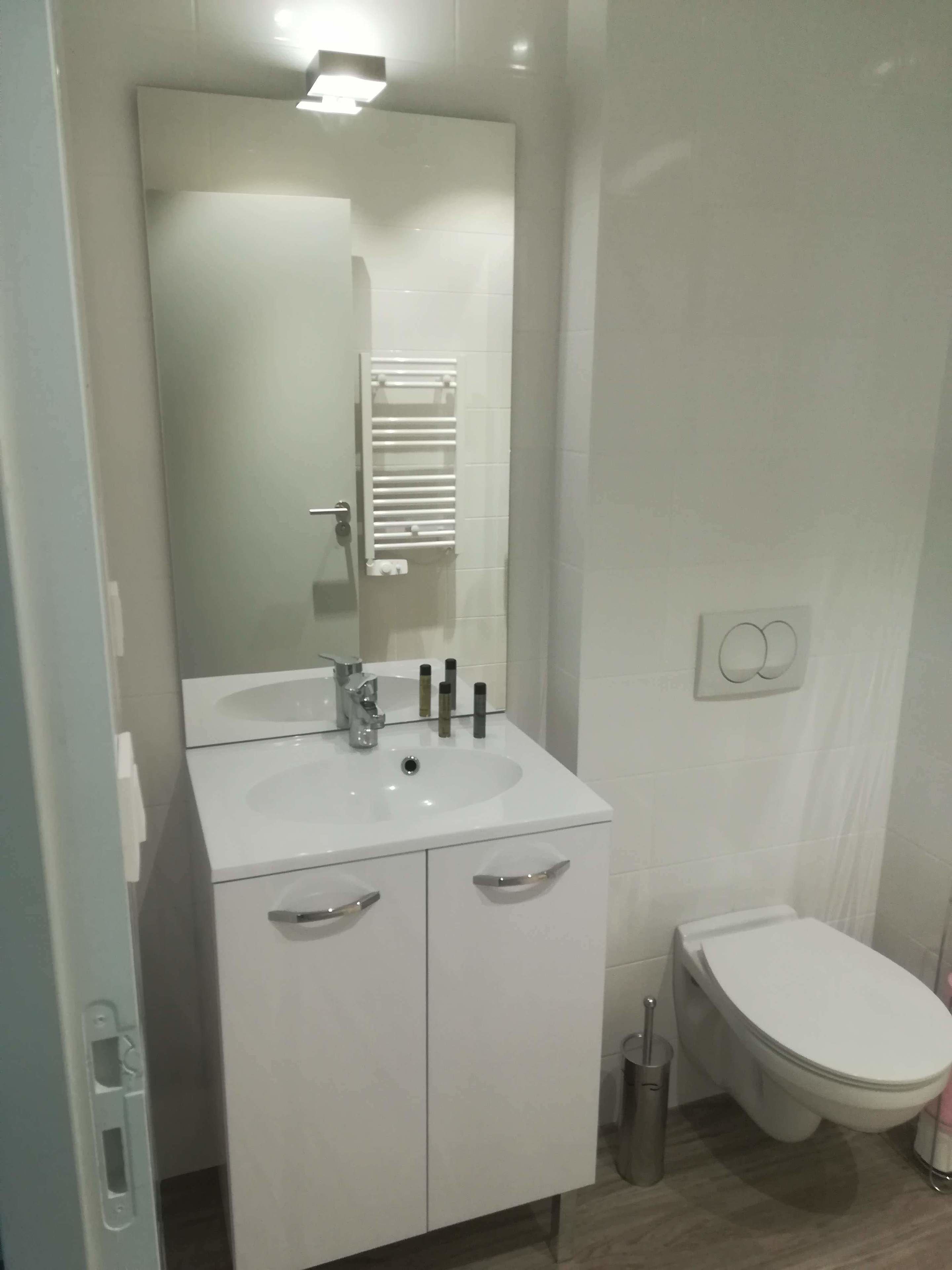 Et moderne badeværelse med hvid vask, spejl og toilet.