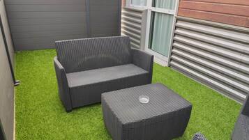 A small outdoor patio area with artificial green turf, a wicker sofa, and a matching ottoman.