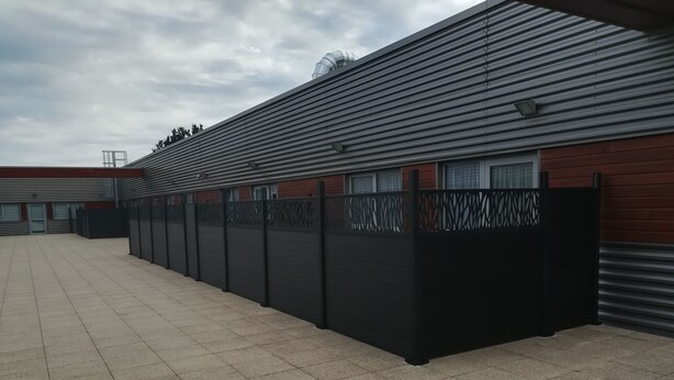 A large industrial building with a flat roof, a long black fence, and a paved area. - ATAO Résidence (Vern-sur-Seiche)