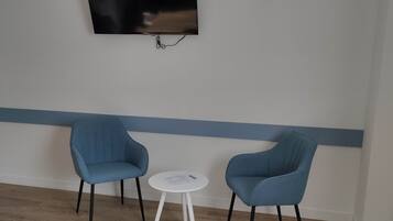 A room with a flat-screen TV mounted on the wall, two blue chairs, and a small white table.
