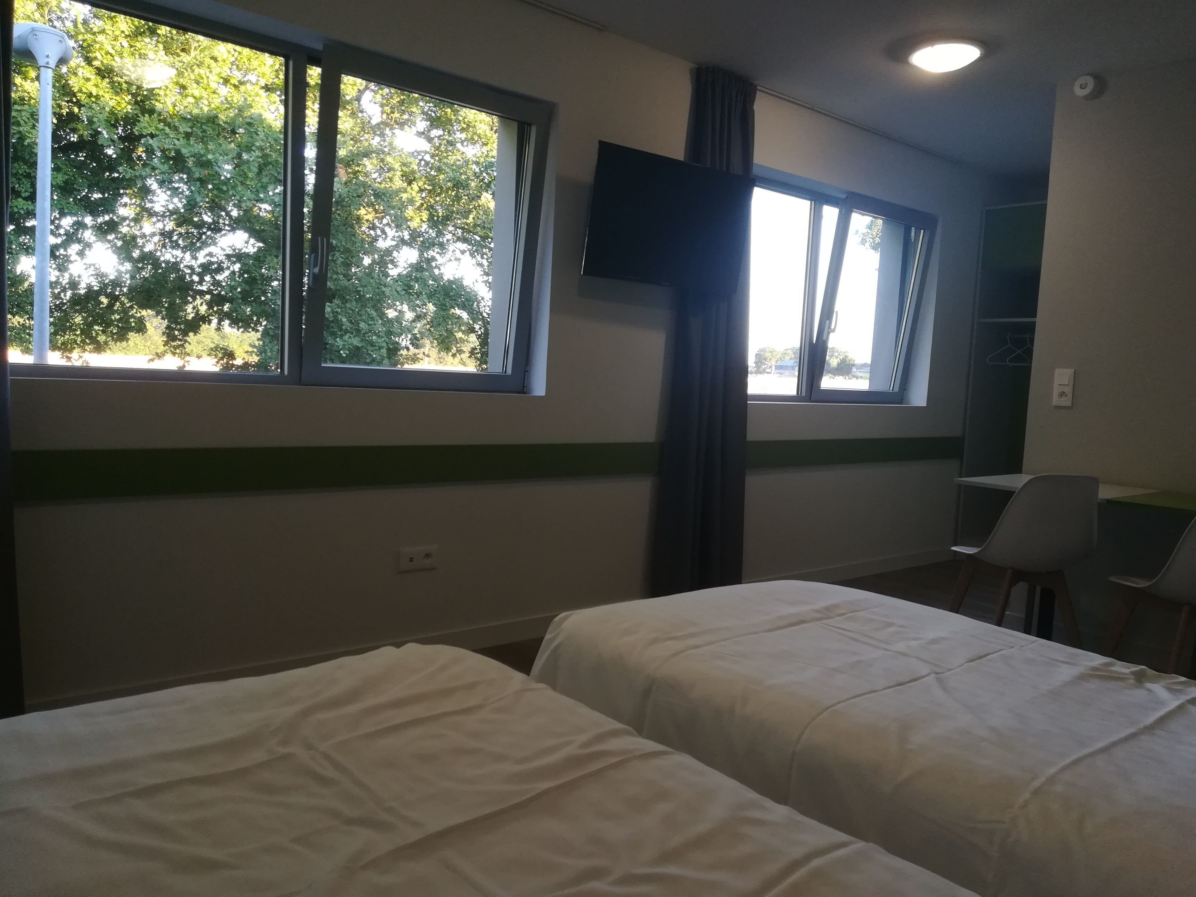 Een kamer met twee bedden, een bureau en een raam met uitzicht op bomen.
