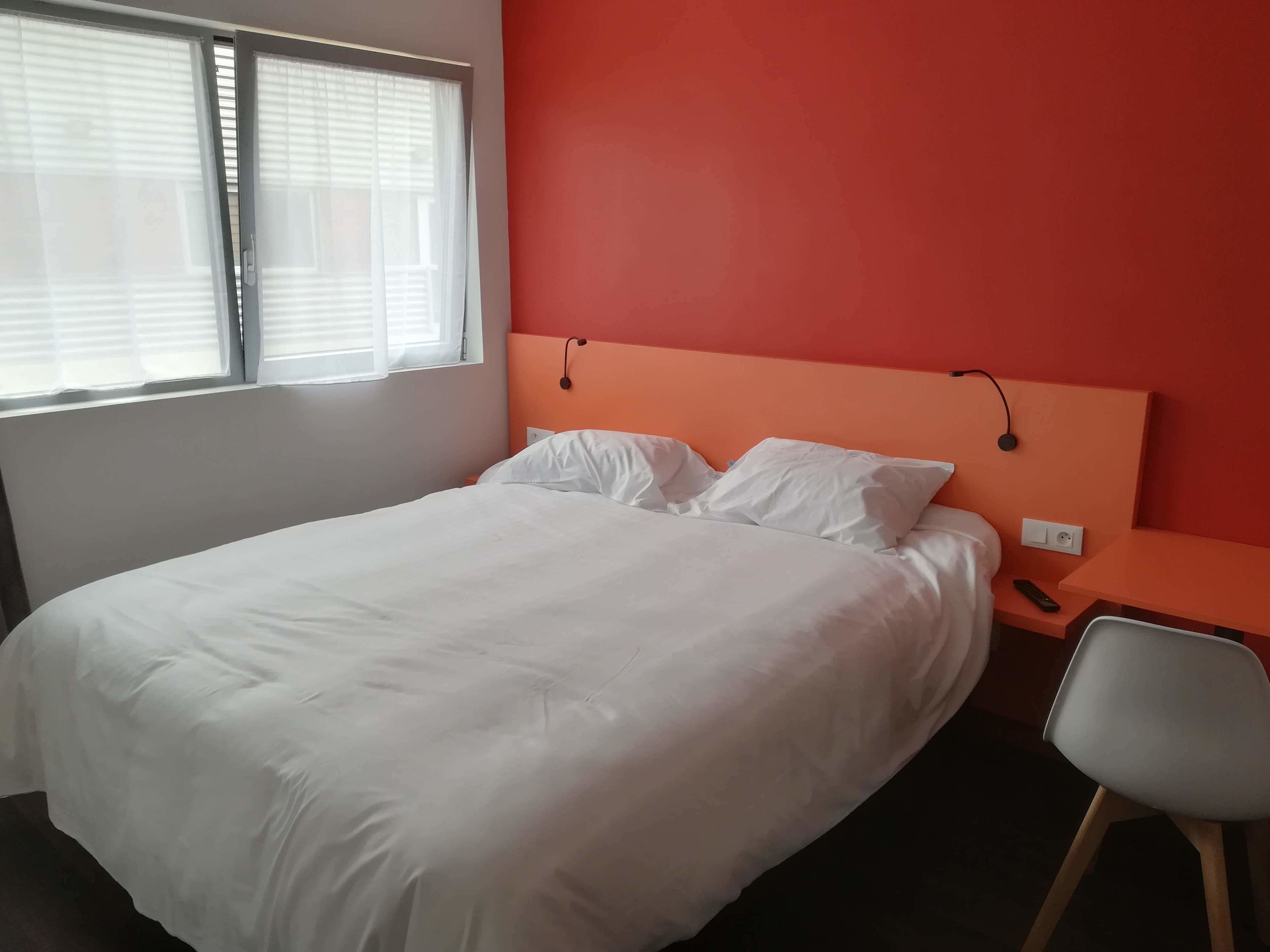 A bedroom with a bed, a nightstand, a chair, and a window with blinds.