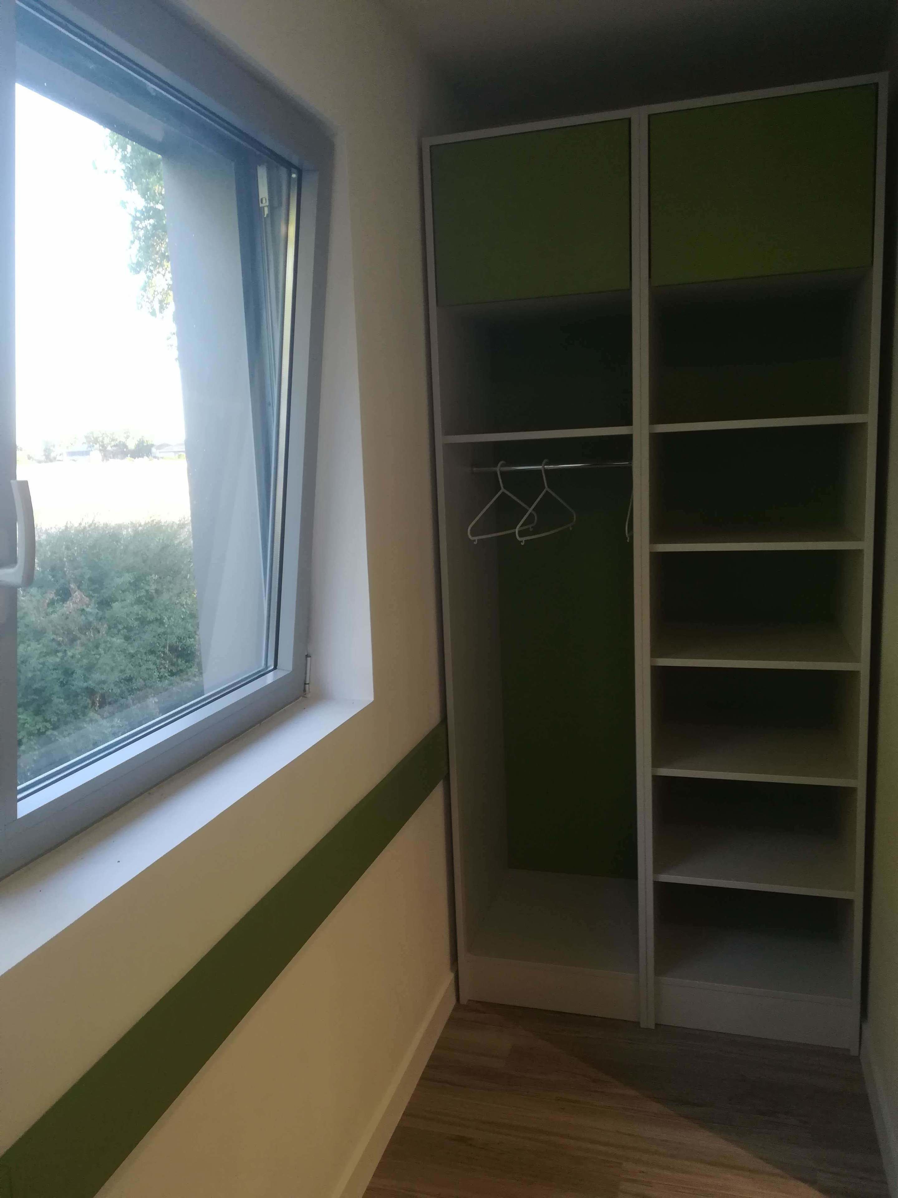 A room with a window, a green and white wardrobe, and a wooden floor.