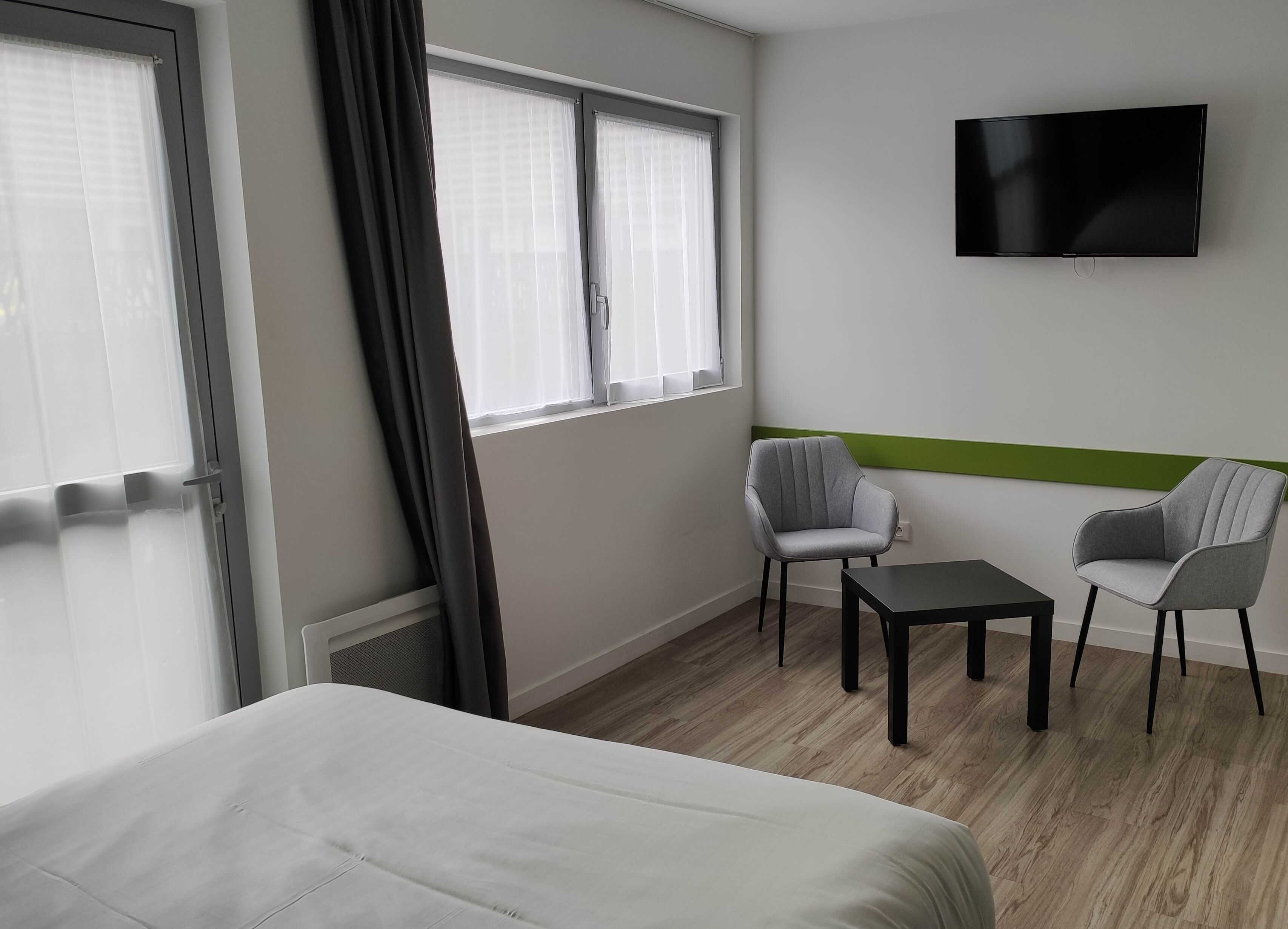 Camera d'albergo con un letto, due poltrone, un tavolino, una televisione a parete e una finestra con tende.
