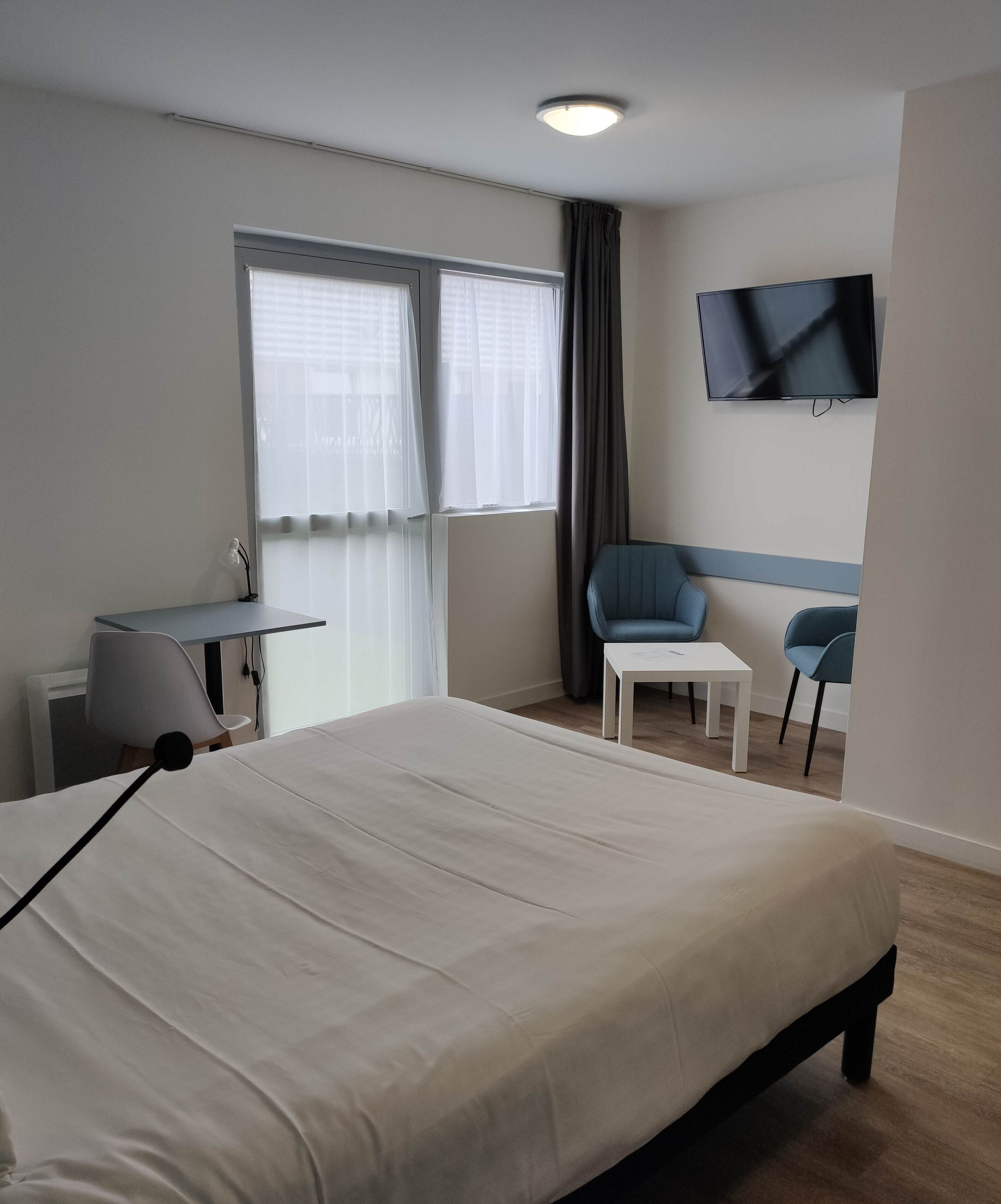 Una habitación de hotel con cama, escritorio, dos sillas, televisor y ventana con cortinas.