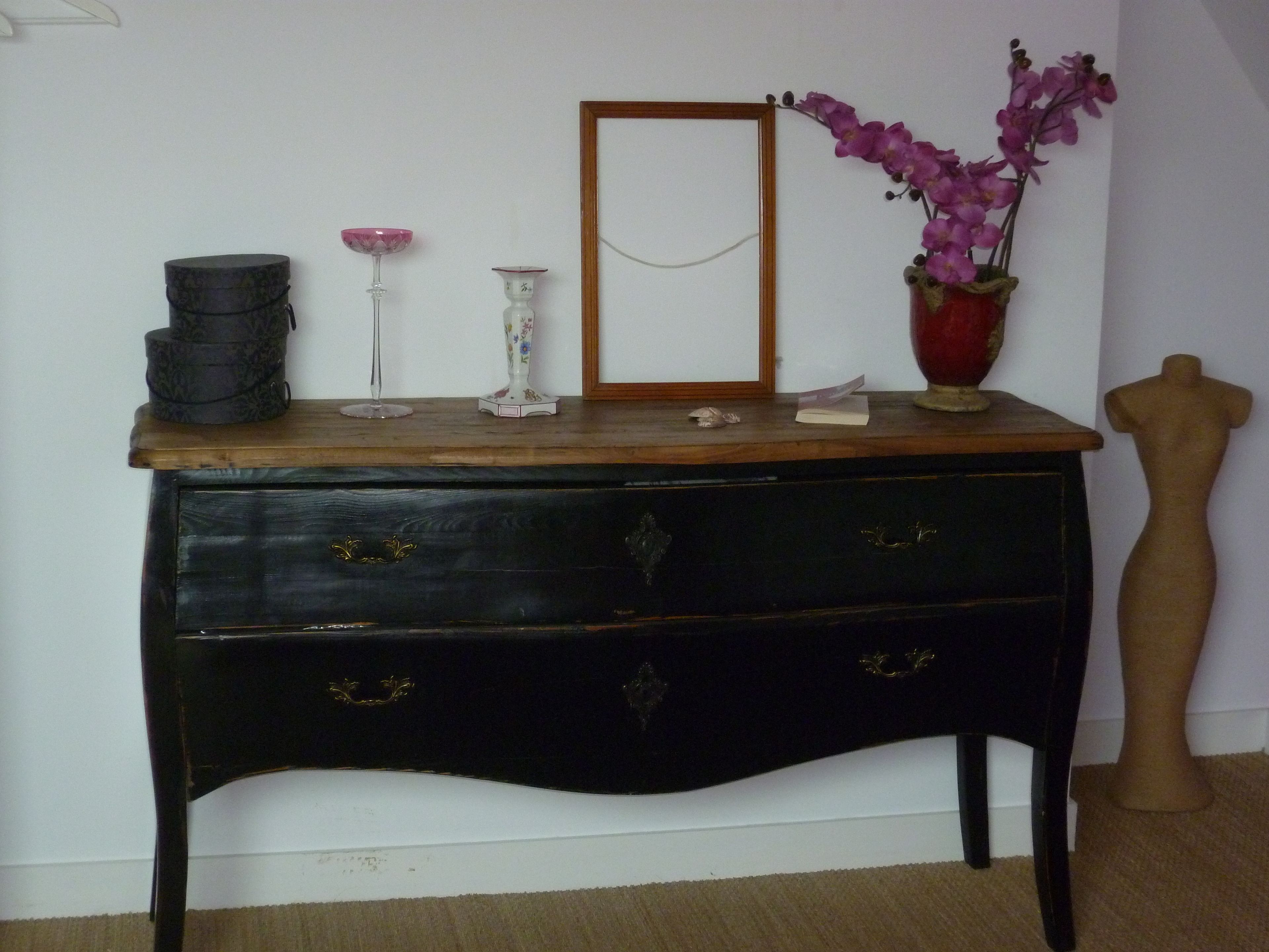 Un aparador de madera antiguo con un espejo, un jarrón con flores moradas y un maniquí.