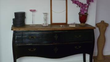 Un aparador de madera antiguo con un espejo, un jarrón con flores moradas y un maniquí.