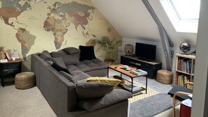 Un salón tipo loft con un mapa del mundo en la pared, un sofá seccional gris, una mesa de centro de madera, una estantería y un tragaluz.