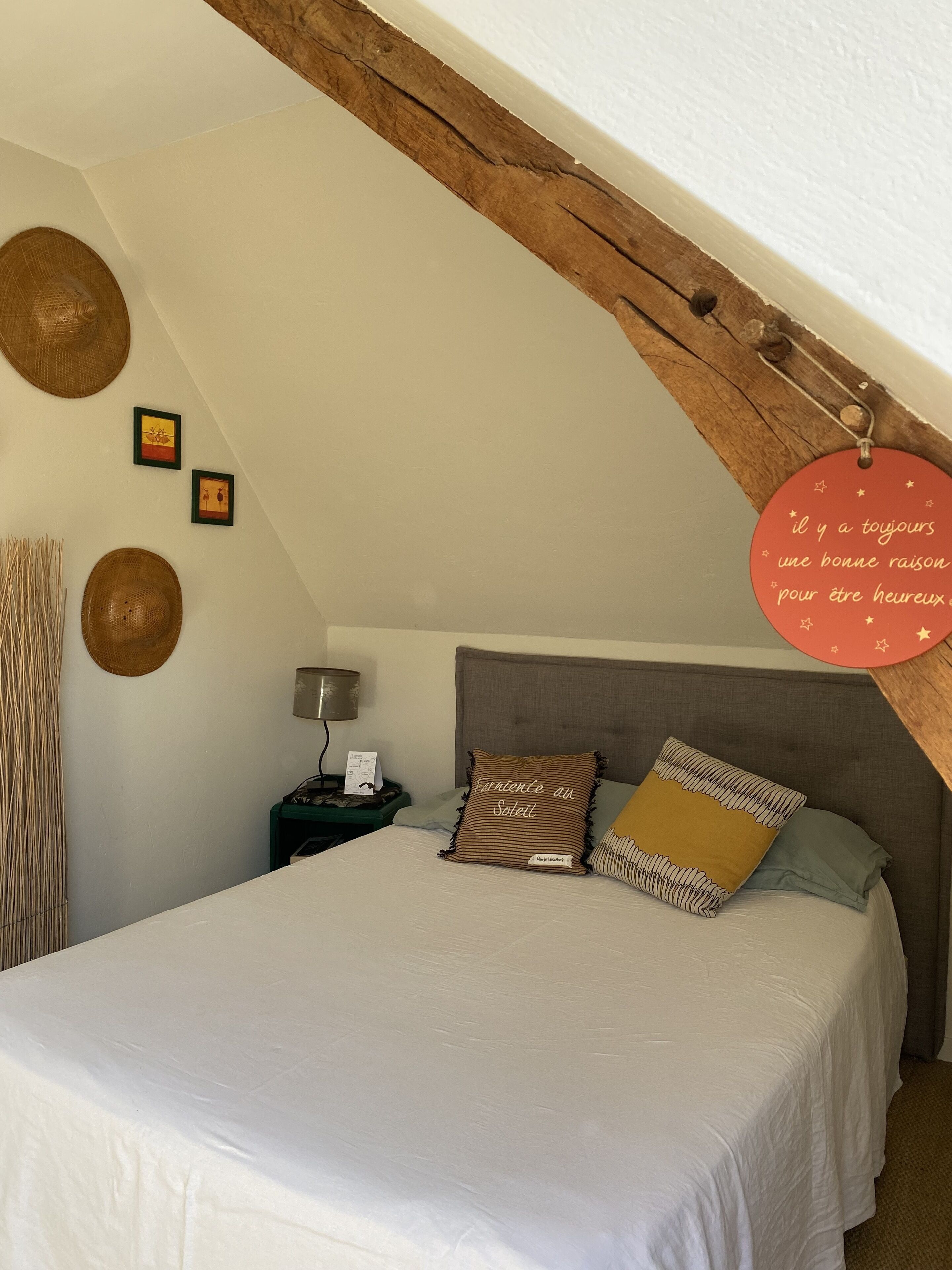 A bedroom with a sloped ceiling, a bed with striped pillows, a nightstand with a lamp, and a wall-mounted sign.