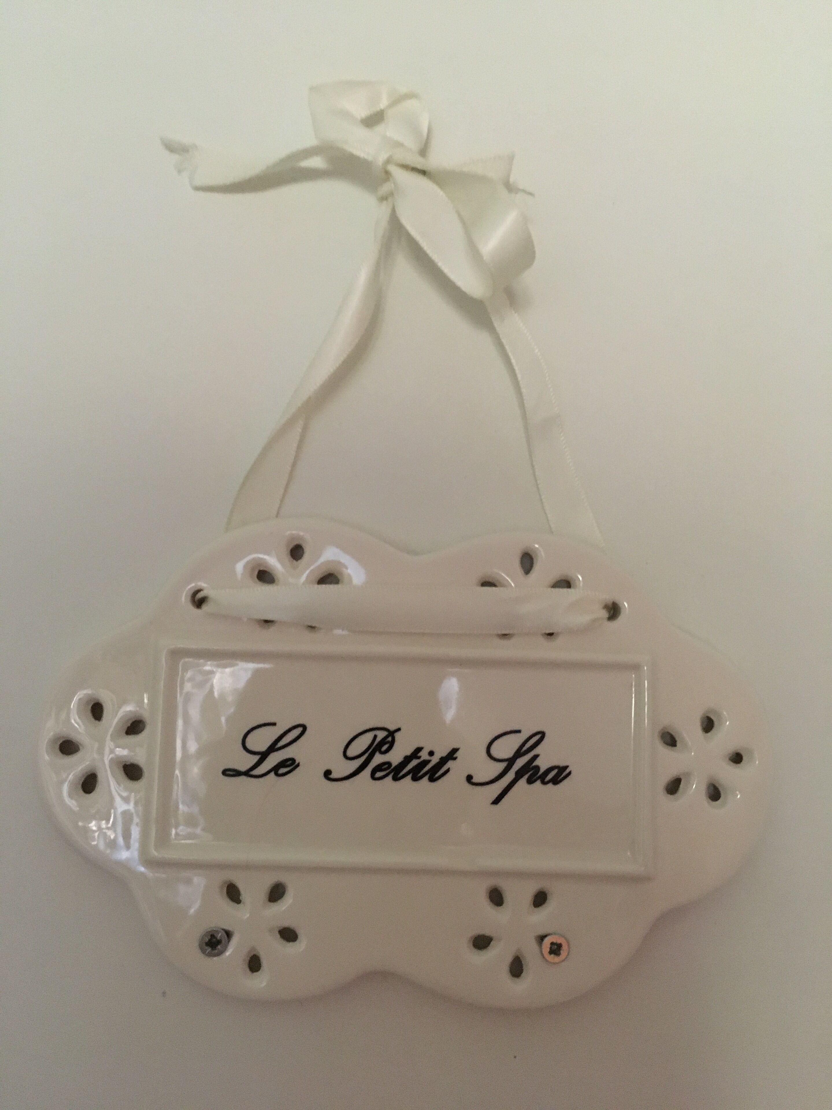 A white ceramic sign with a ribbon, featuring the text "Le Petit Spa".