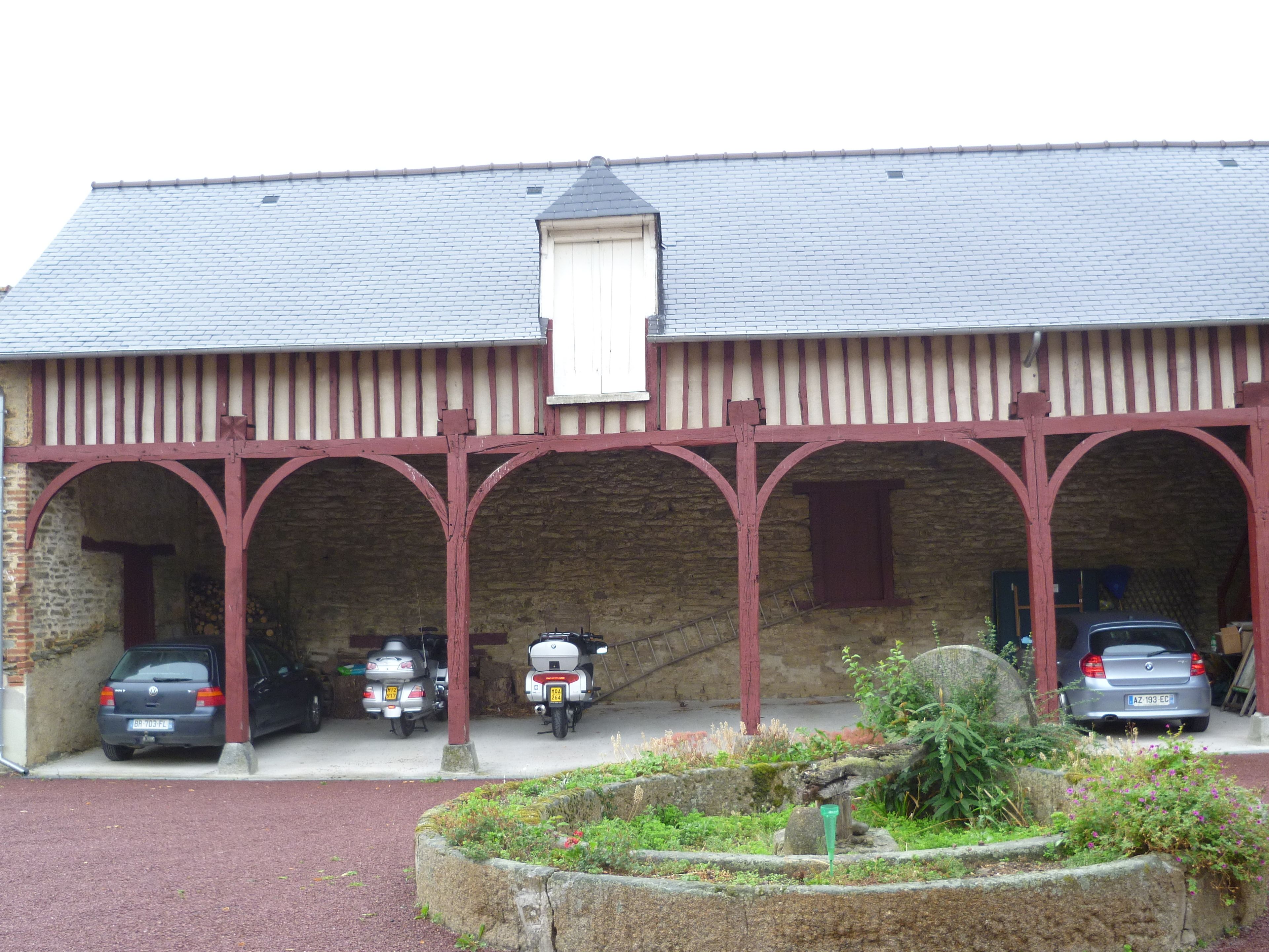 Un edificio con fachada de piedra y un porche cubierto con vigas rojas. Hay coches y una motocicleta estacionados frente a él.