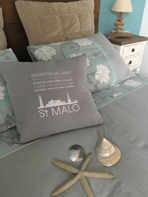 A bed with a pillow featuring a cityscape and text, a starfish, and a seashell. - Chambre d'hôtes La Métairie à Domloup (Domloup)