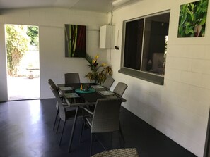 A dining area with a table and chairs, a potted plant, and a window with a view of greenery. - Egrets Rest - Daintree (Daintree)