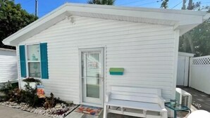 A small white building with a single door and a small bench outside. - SURF SHACK (Cape Canaveral)